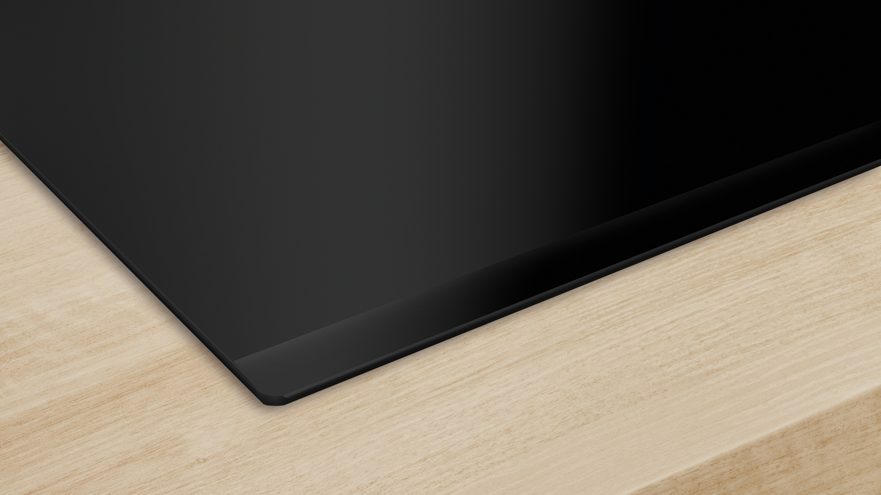 Zbliżenie czarnej, płaskiej, błyszczącej płyty grzewczej na jasnym drewnianym blacie.