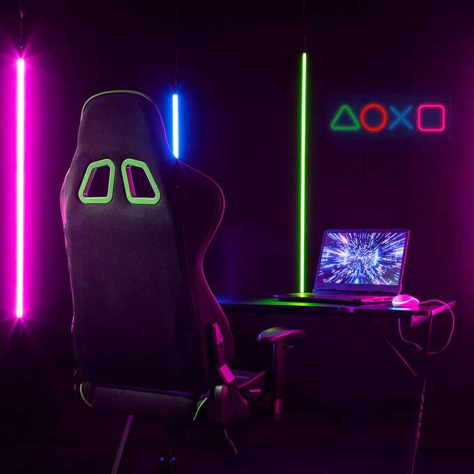 Krzesło do gier, laptop, neonowe światła i symbol kontrolera PlayStation na ścianie w ciemnym pokoju.