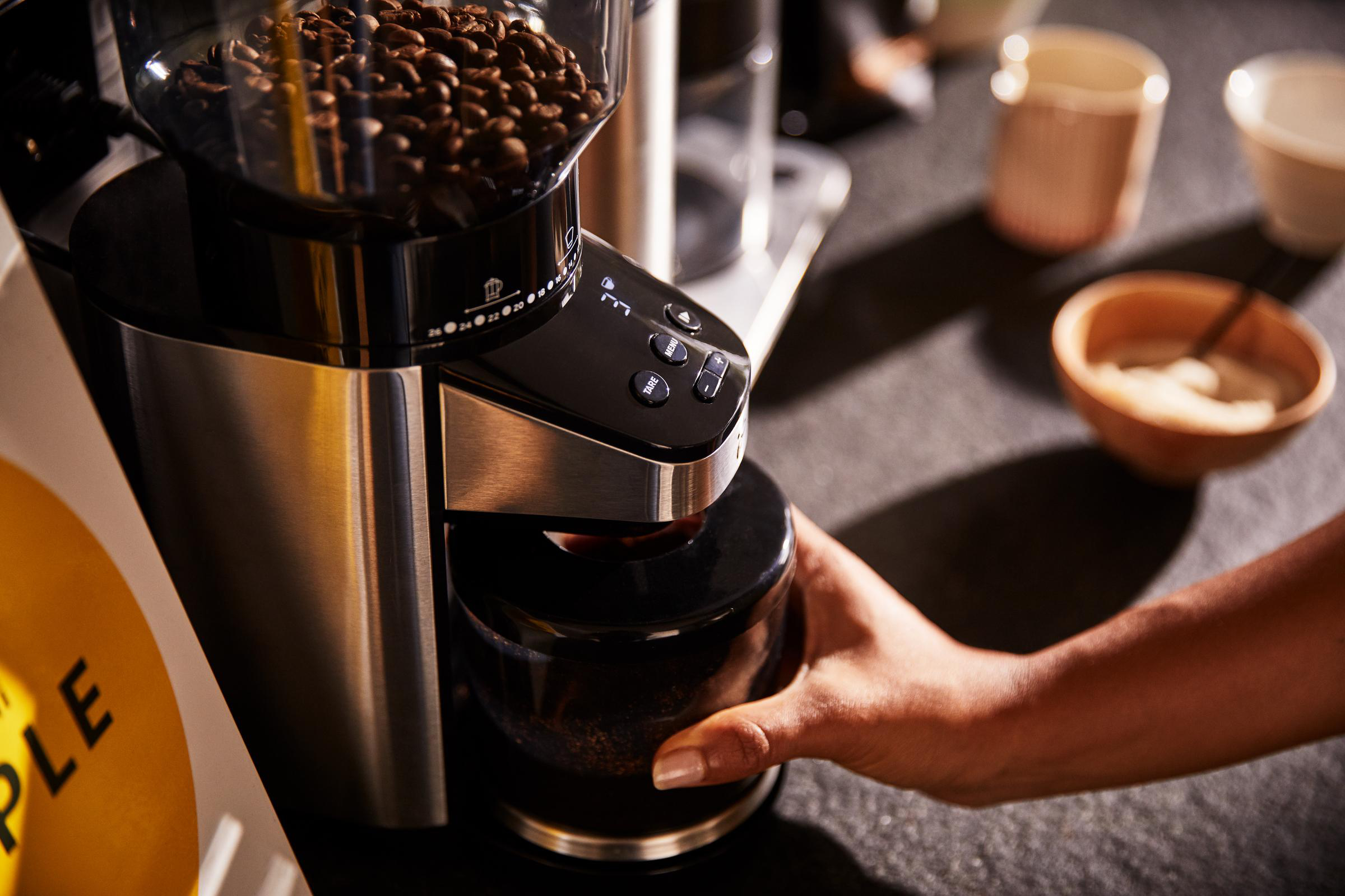 Person gießt gemahlenen Kaffee aus einer Kaffeemühle in ein schwarzes Glas.