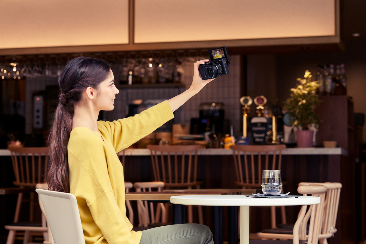 Eine Frau macht in einem Café ein Selfie mit einer Kamera; verschwommener Hintergrund.