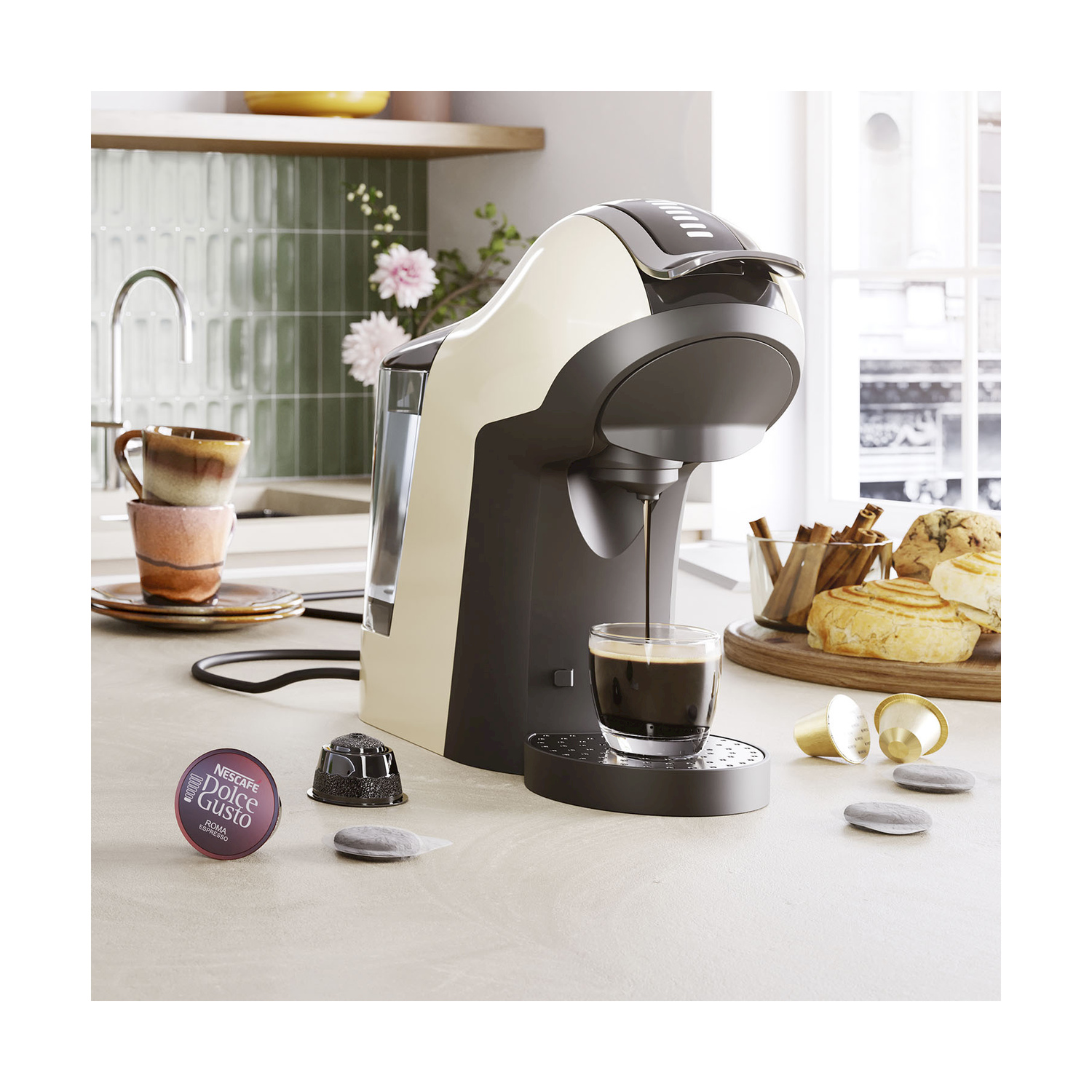 Caffettiera che versa caffè in un bicchiere. Tazze, cialde e cibo sul bancone. Sfondo cucina.