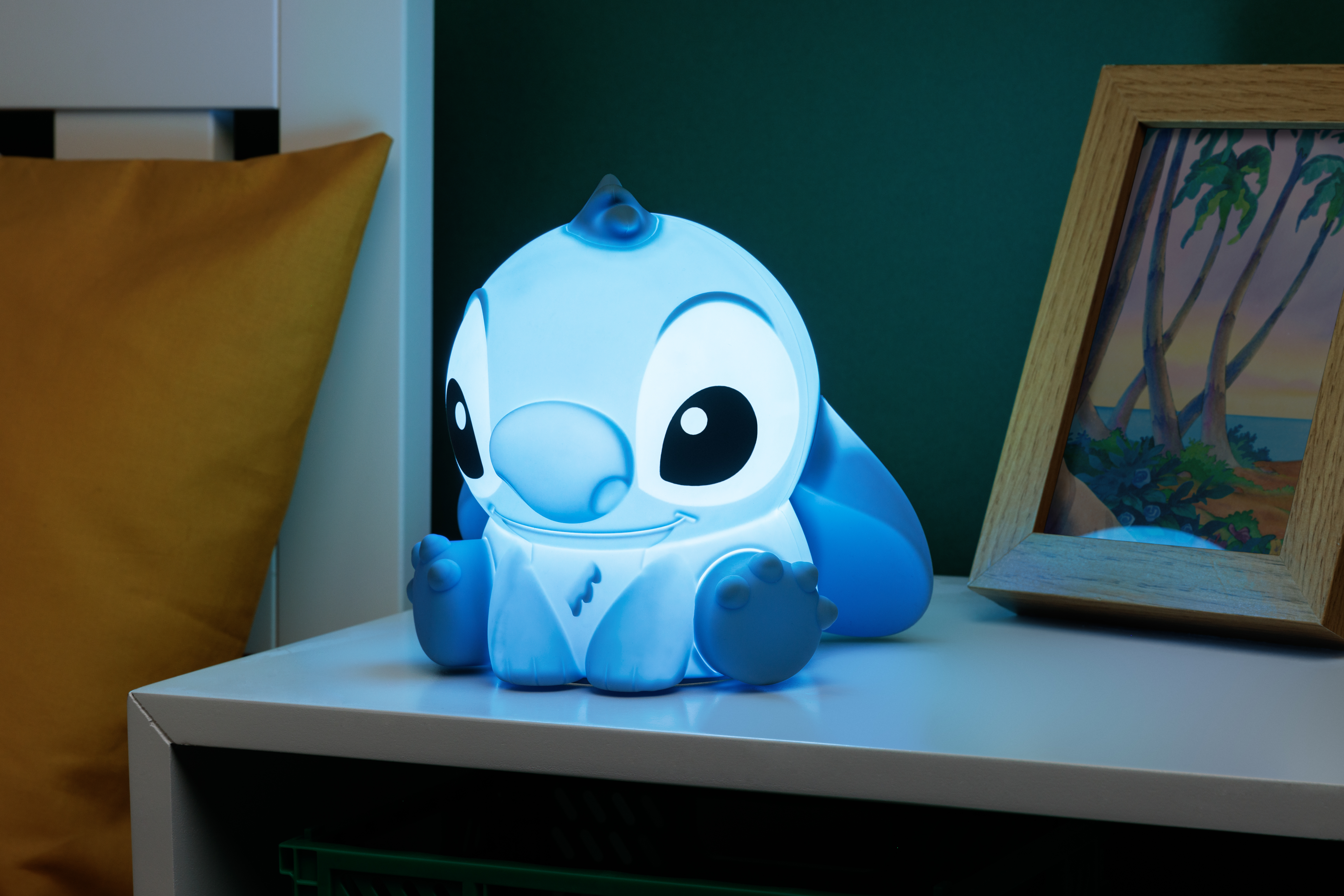 Blaue Stitch-Lampe auf weißer Oberfläche, mit blauem Licht beleuchtet, mit einem gerahmten Bild im Hintergrund.