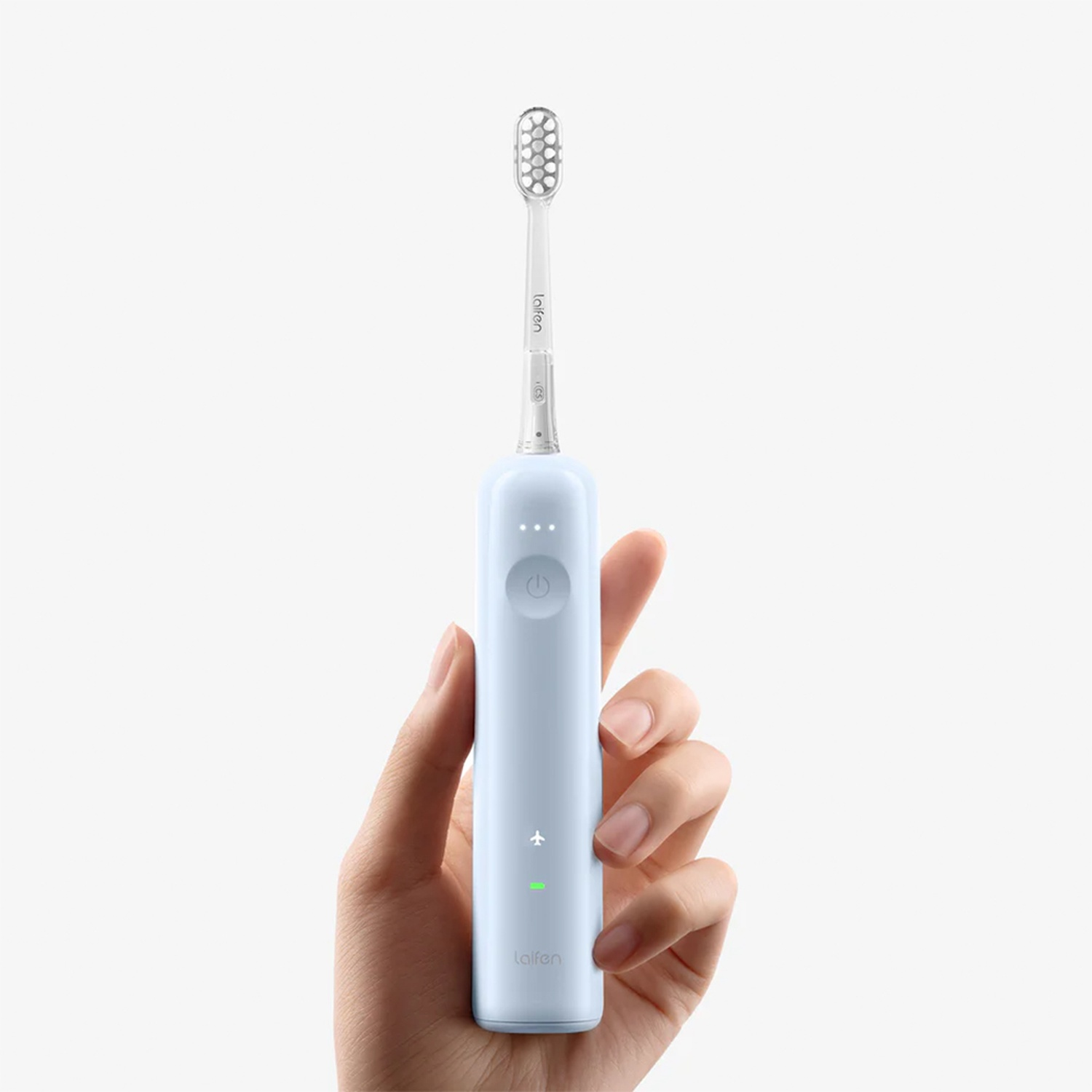 Spazzolino elettrico azzurro nella mano di una persona. Sfondo bianco.