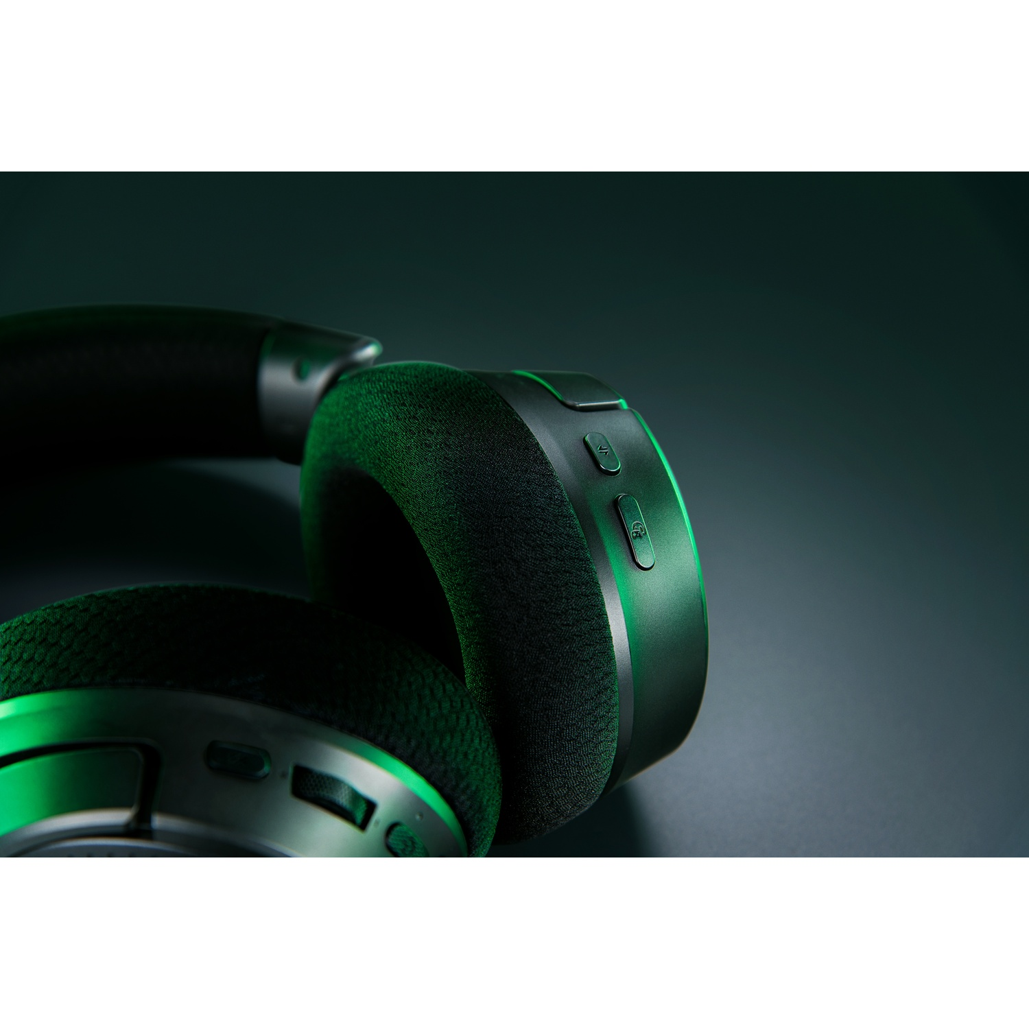 Gros plan sur un casque noir avec des accents verts. Boutons et coussinets d'oreille visibles sur fond sombre.