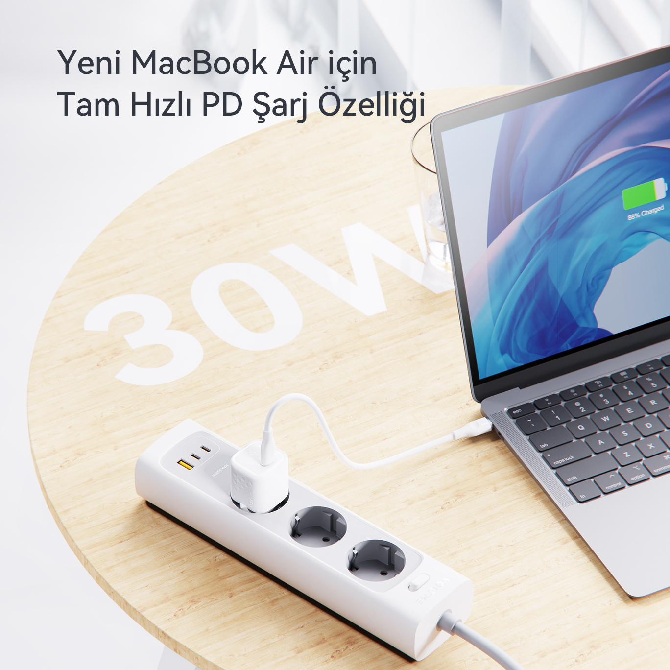Ahşap bir masa üzerinde bir dizüstü bilgisayar ve şarj kablosu olan bir priz.