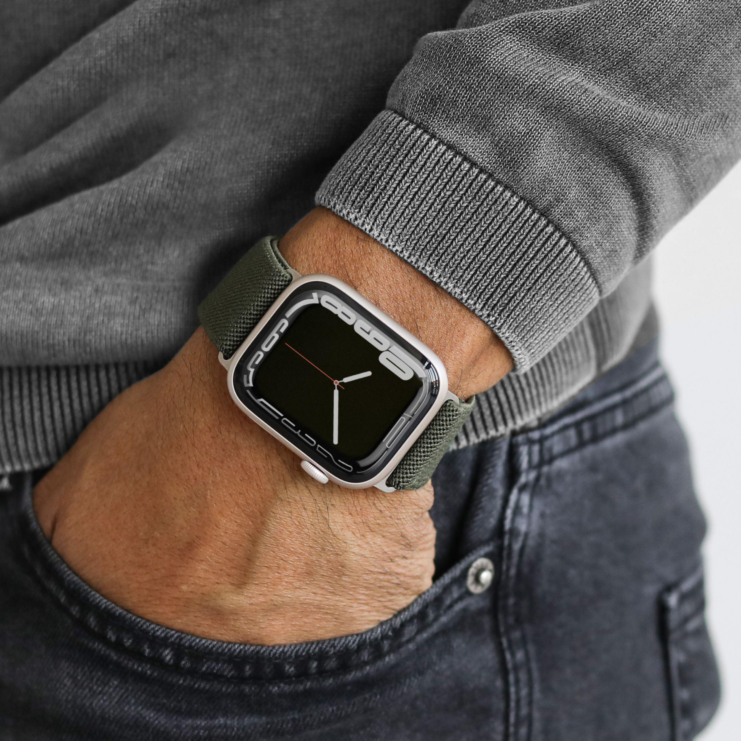 Handgelenk mit grüner Uhr und grauem Pullover.