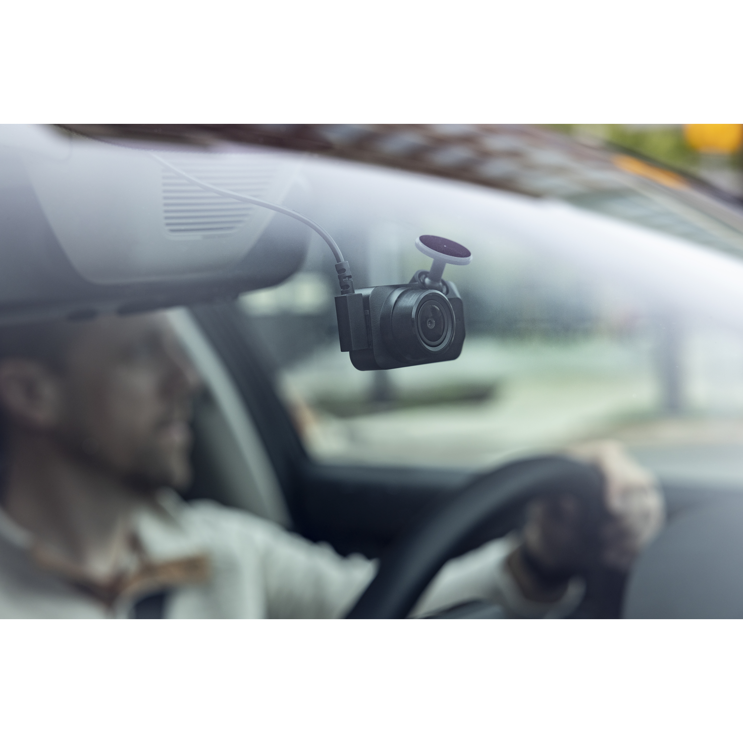 Dashcam gemonteerd op voorruit, met een man op de wazige achtergrond die een auto bestuurt.