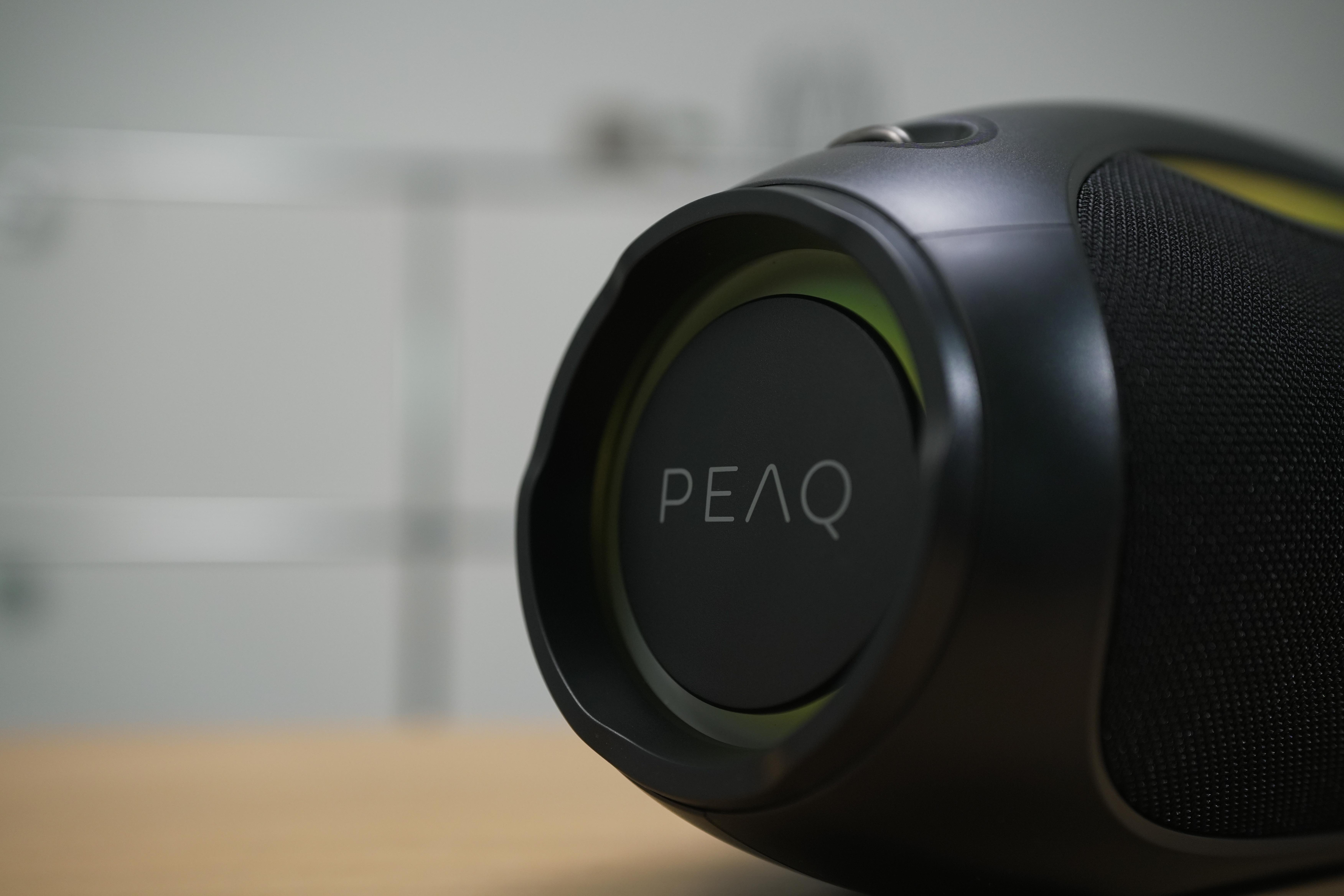 Nahaufnahme eines schwarzen Lautsprechers mit dem Wort "PEAQ" auf der Seite, verschwommener Hintergrund.