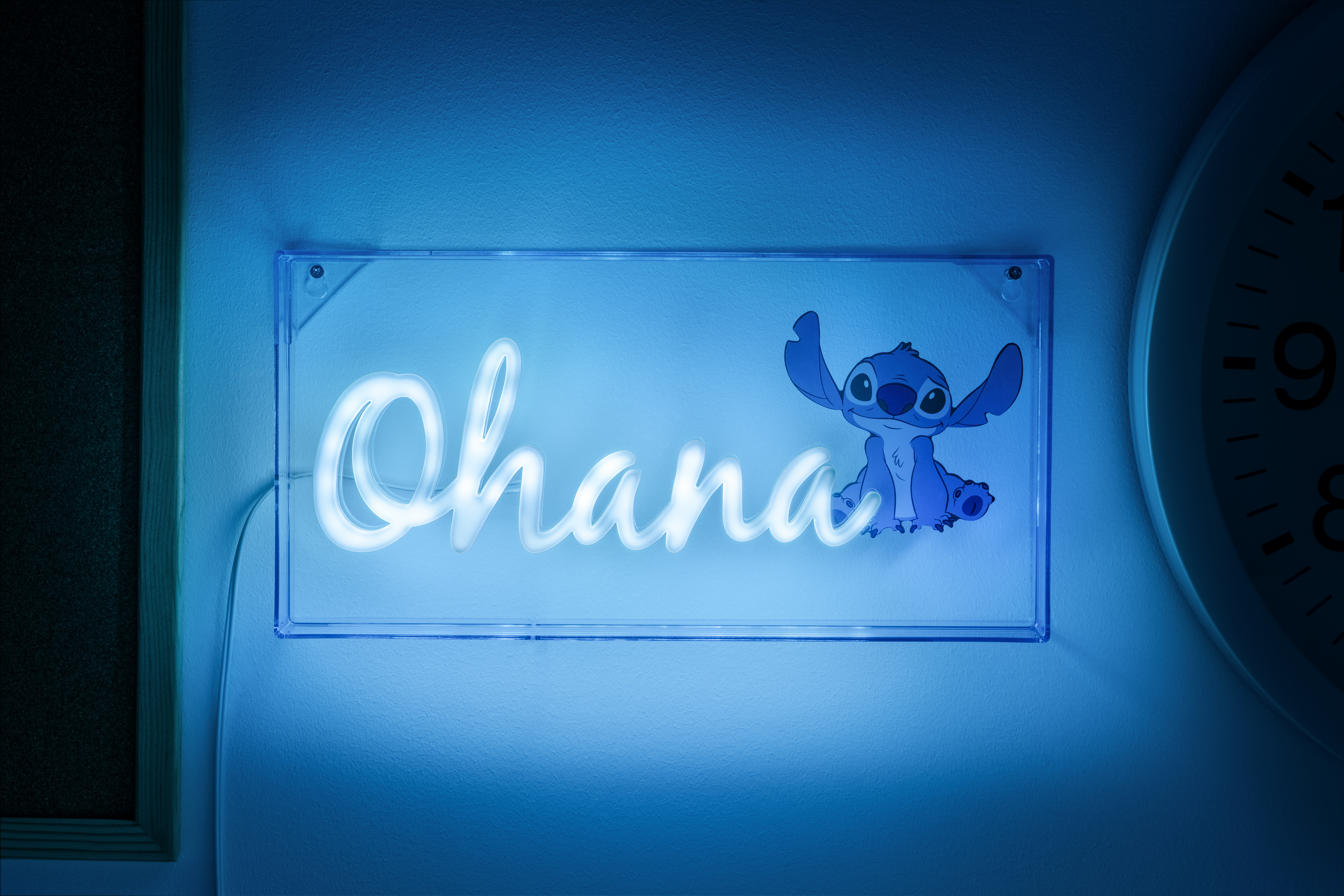 Blaues Neon-Schild an einer Wand mit 'Ohana' und Stitch-Figur. Im Hintergrund eine Uhr.