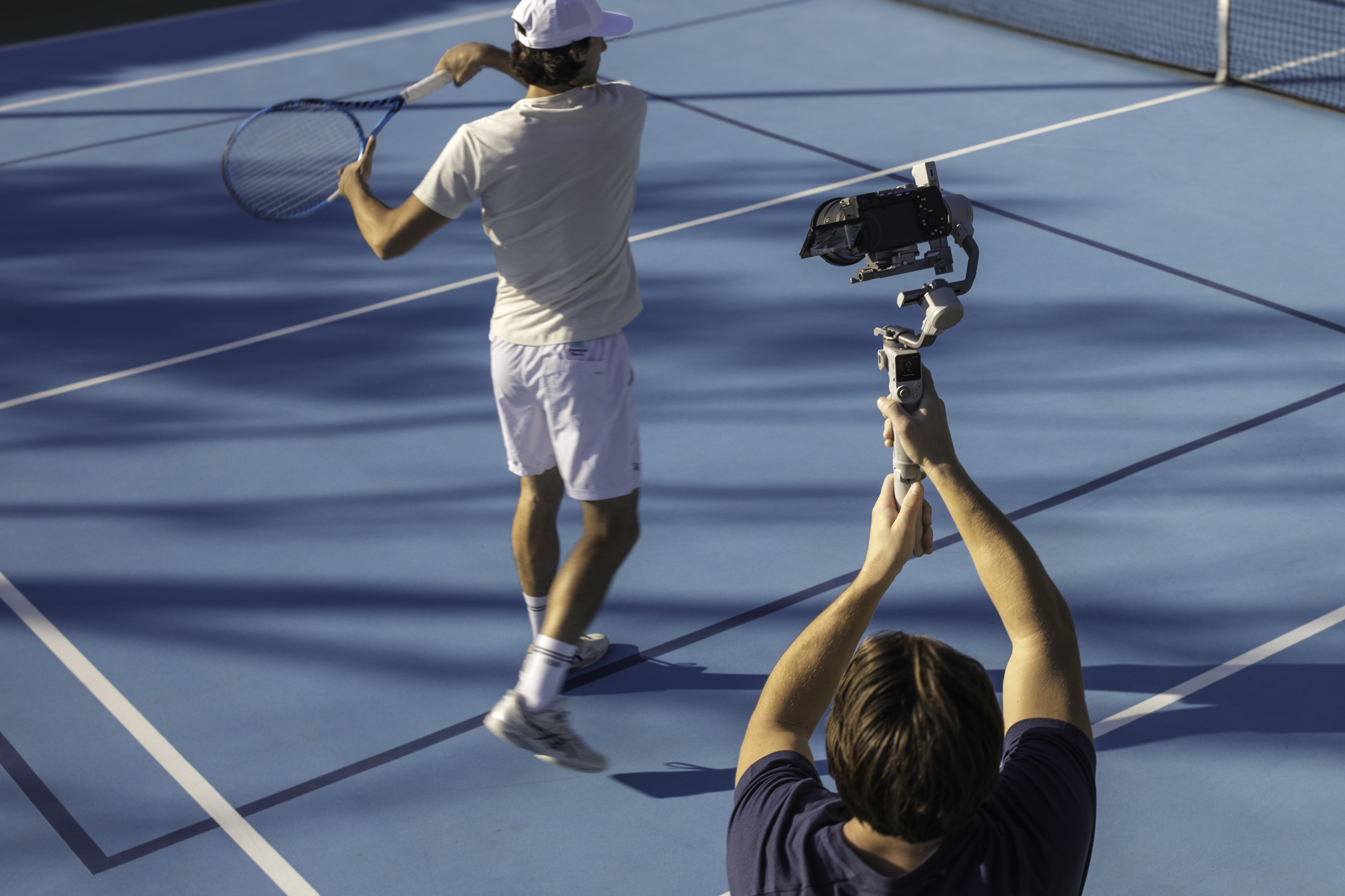 Eine Person filmt einen Tennisspieler auf einem blauen Platz mit einem Gimbal.