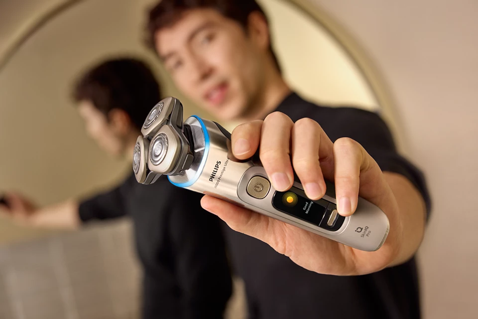 Férfi elektromos borotvát tart a fürdőszobában.