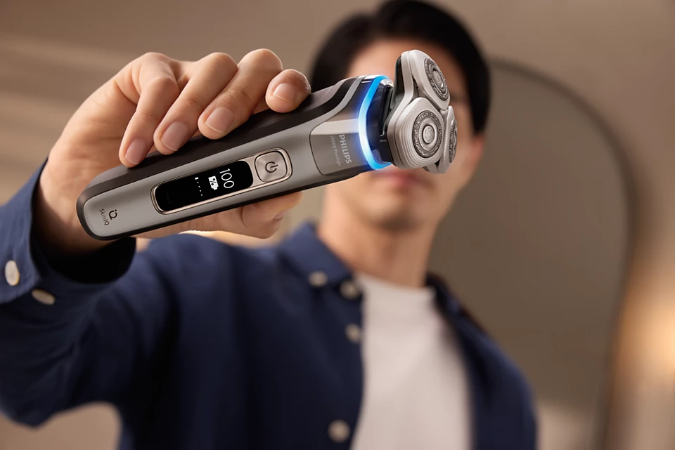 Férfi egy Philips elektromos borotvát tart. A borotván három forgófej van.