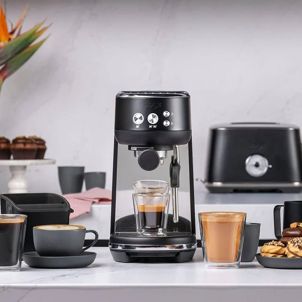 Máquina de espresso negra con café. Tostadora, tazas y pasteles en encimera de mármol.