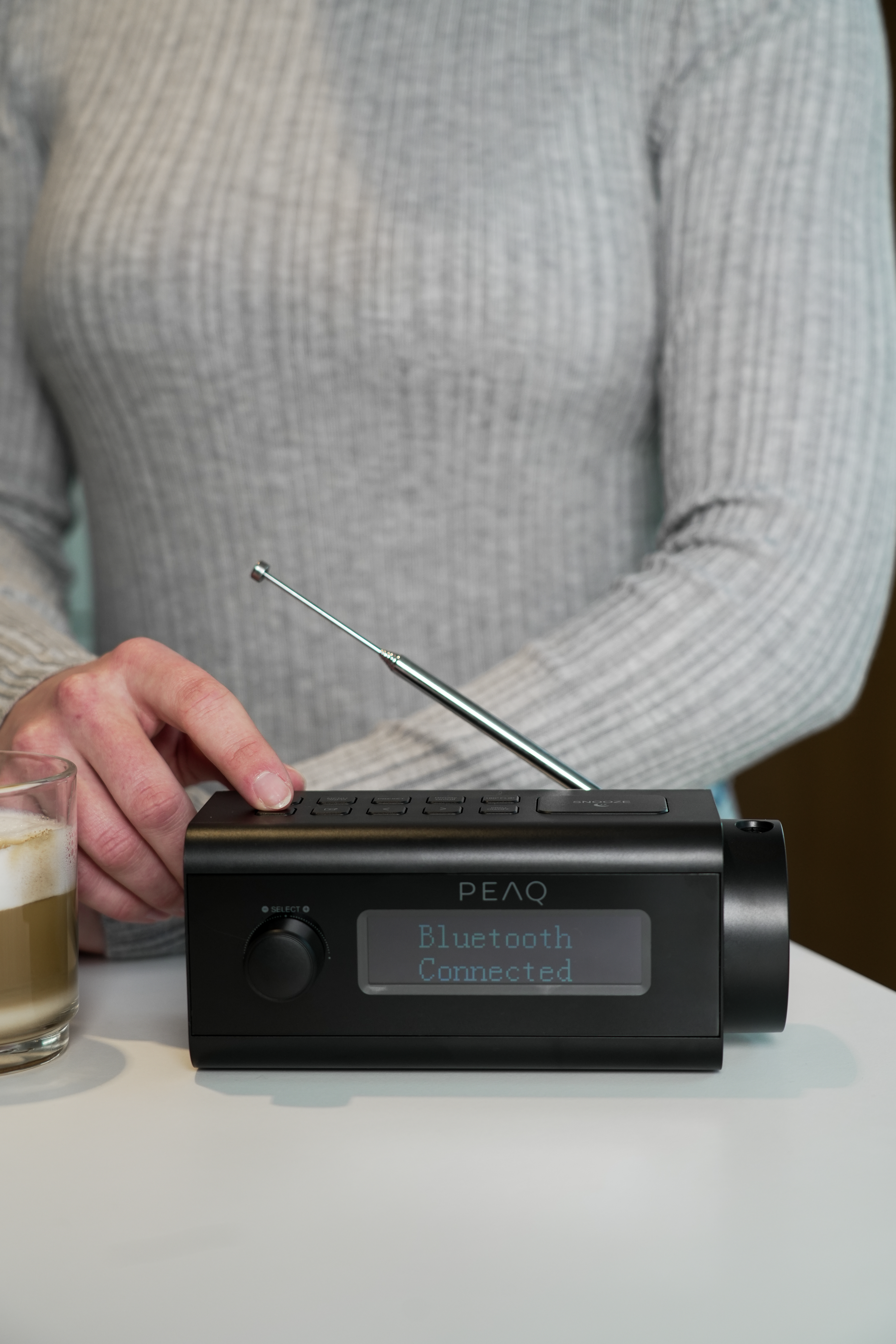 Person bedient schwarzes PEAQ-Radio. Anzeige zeigt 'Bluetooth Connected'.