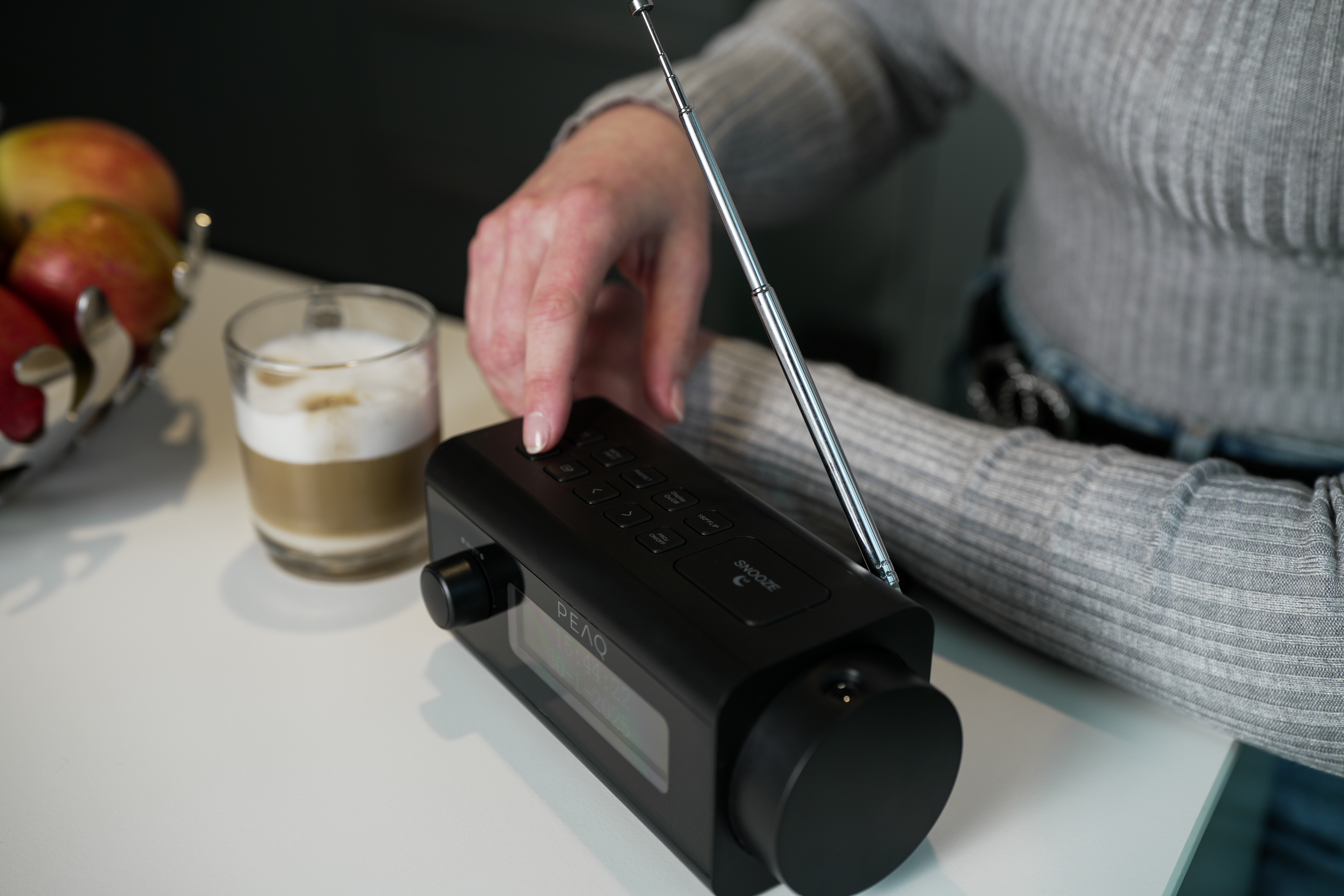 Die Hand einer Person stellt den Lautstärkeregler eines schwarzen Radios mit Antenne ein.