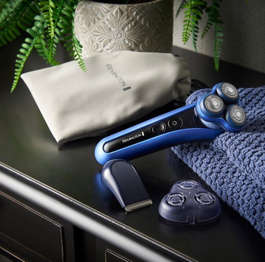 Niebiesko-czarna golarka elektryczna z akcesoriami na ciemnej powierzchni, zieleń w tle.