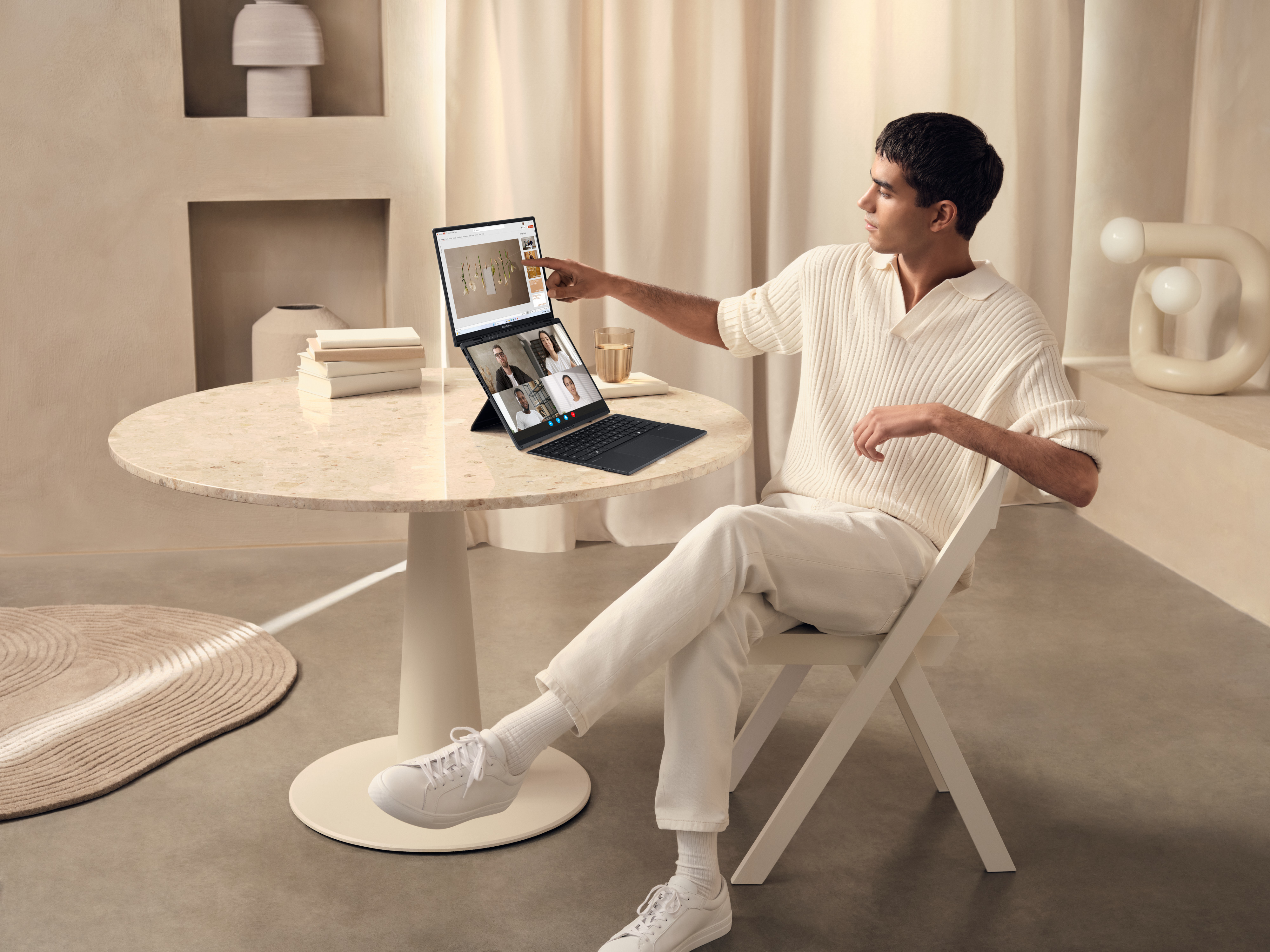 Ein Mann zeigt auf einen Laptop-Bildschirm, der einen Videoanruf zeigt, sitzt an einem Tisch.