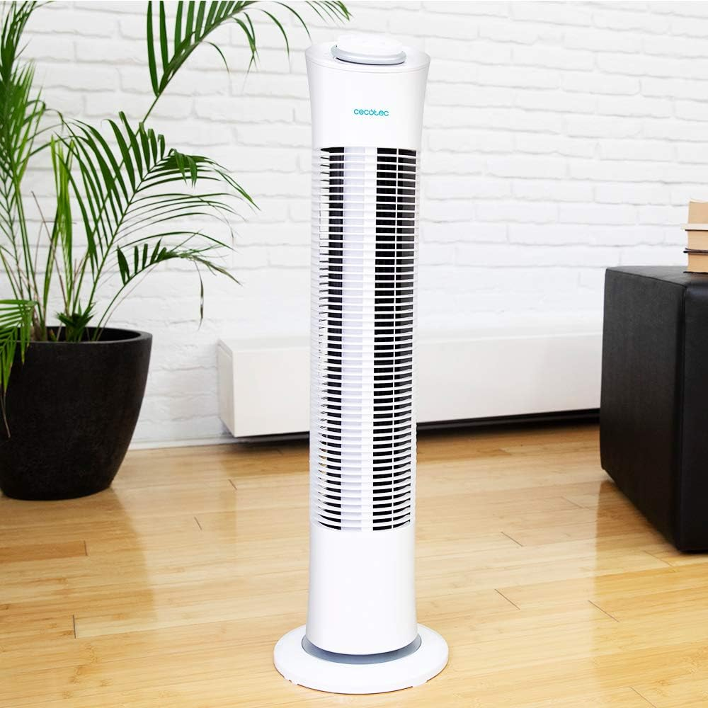 Ventilador de torre blanco en una habitación con planta, pared de ladrillo, suelo de madera y decoración negra.