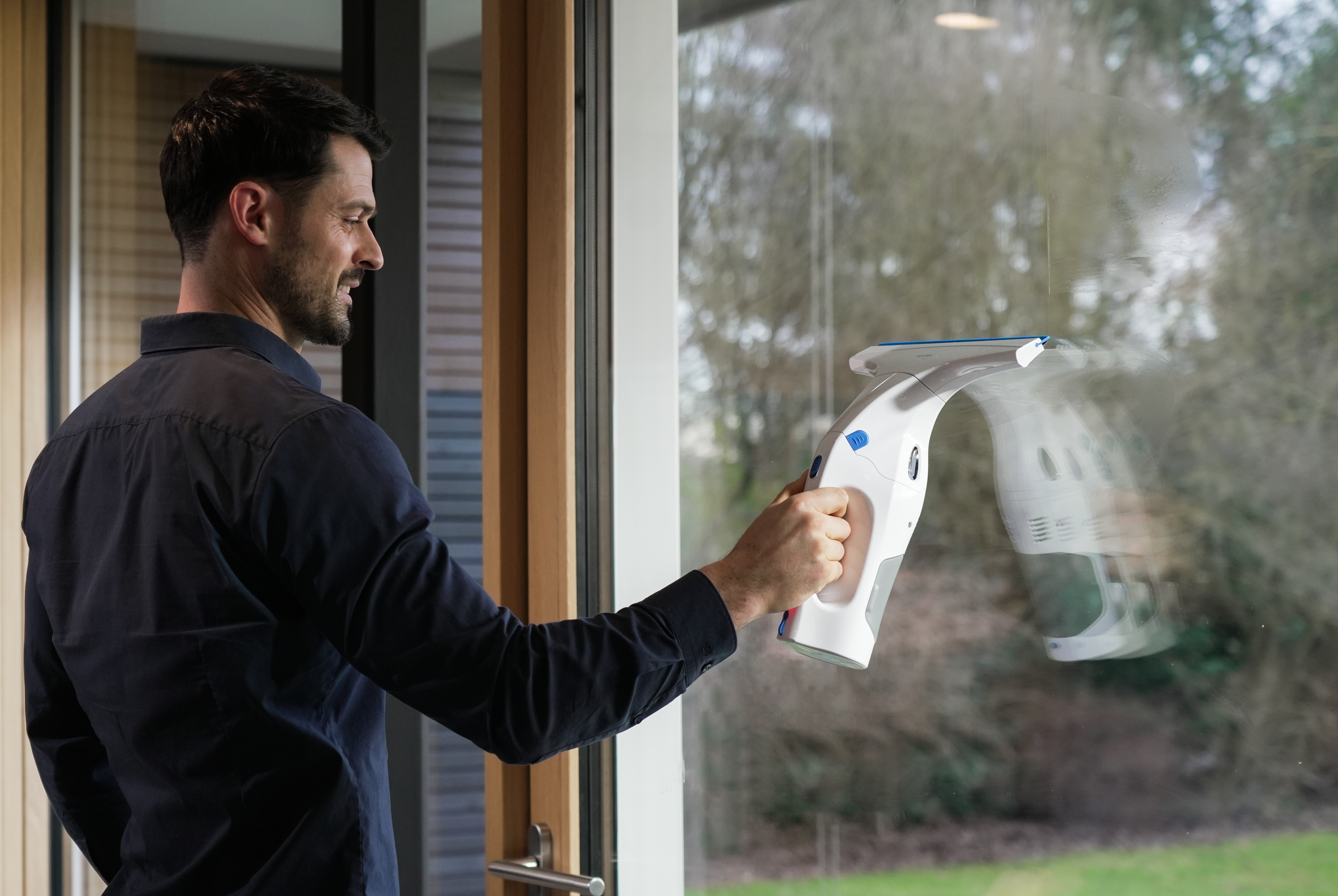 Ein Mann putzt ein Fenster mit einem Abzieher. Außenansicht ist sichtbar.