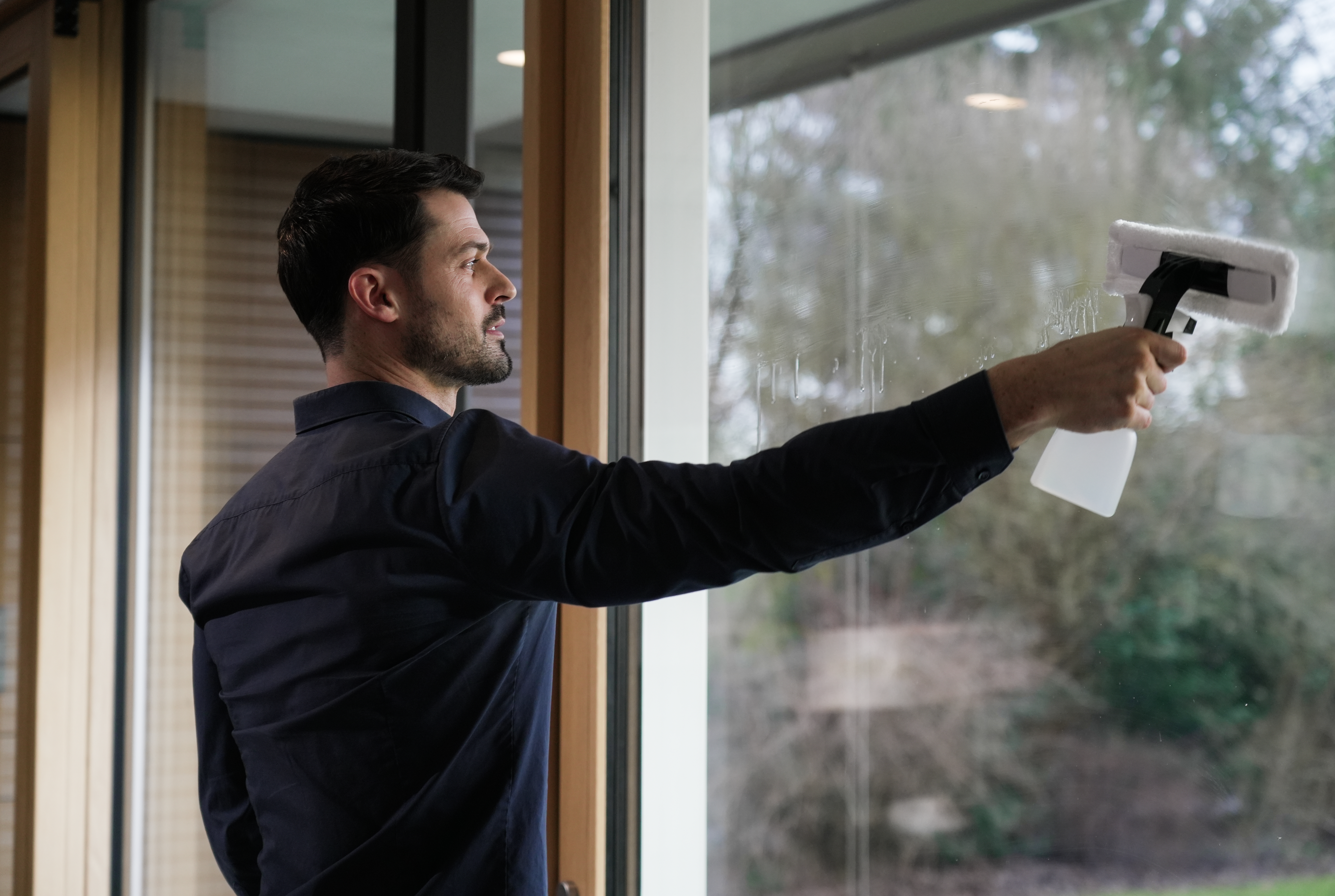 Ein Mann, der ein Fenster mit einem Abzieher reinigt, unscharfer Hintergrund der Außenansicht.