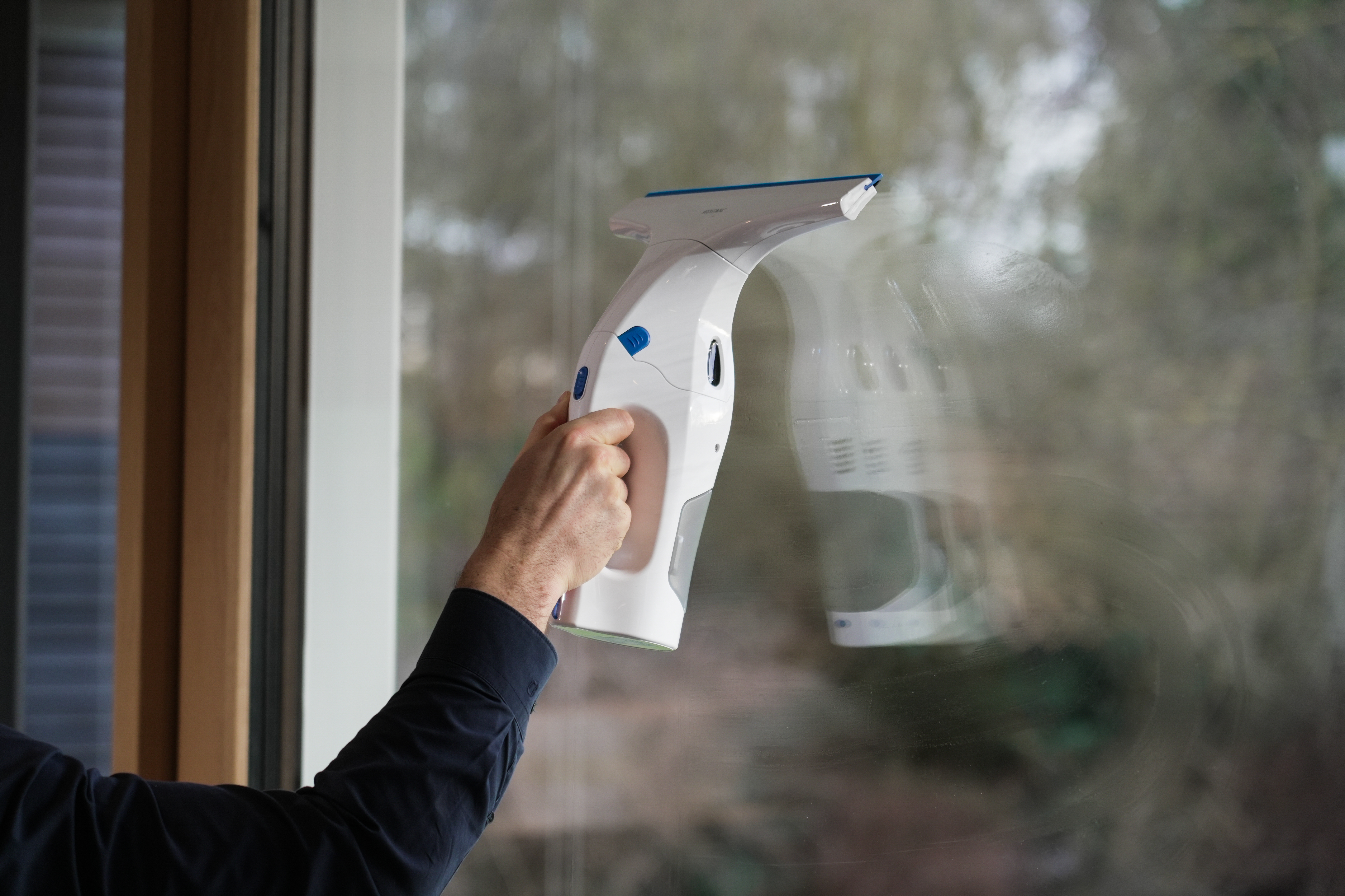 Eine Person, die einen weißen Fensterreiniger verwendet, um ein Fenster zu reinigen, mit einer Spiegelung des Reinigers.