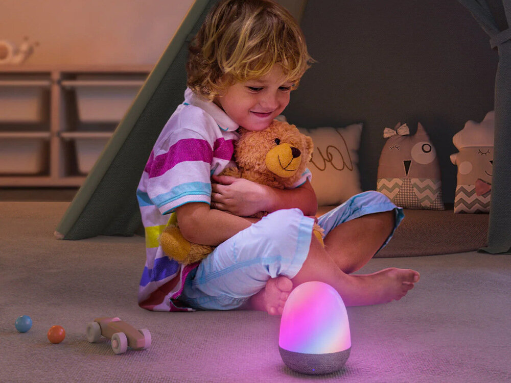 Dziecko przytulające misia, z kolorową lampą w pobliżu w przytulnym pokoju.