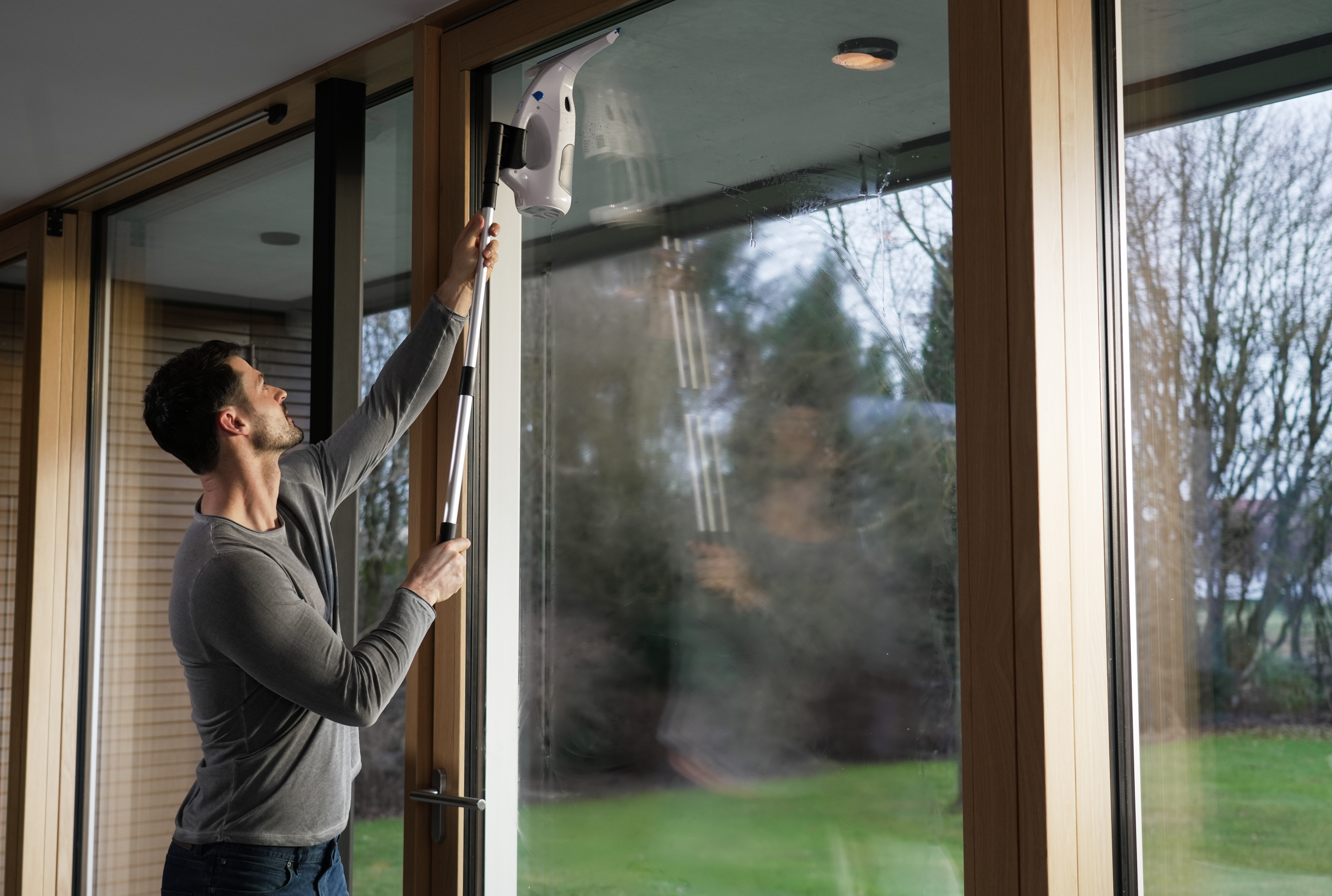 Ein Mann reinigt ein Fenster mit einem Fensterreiniger mit langem Griff.