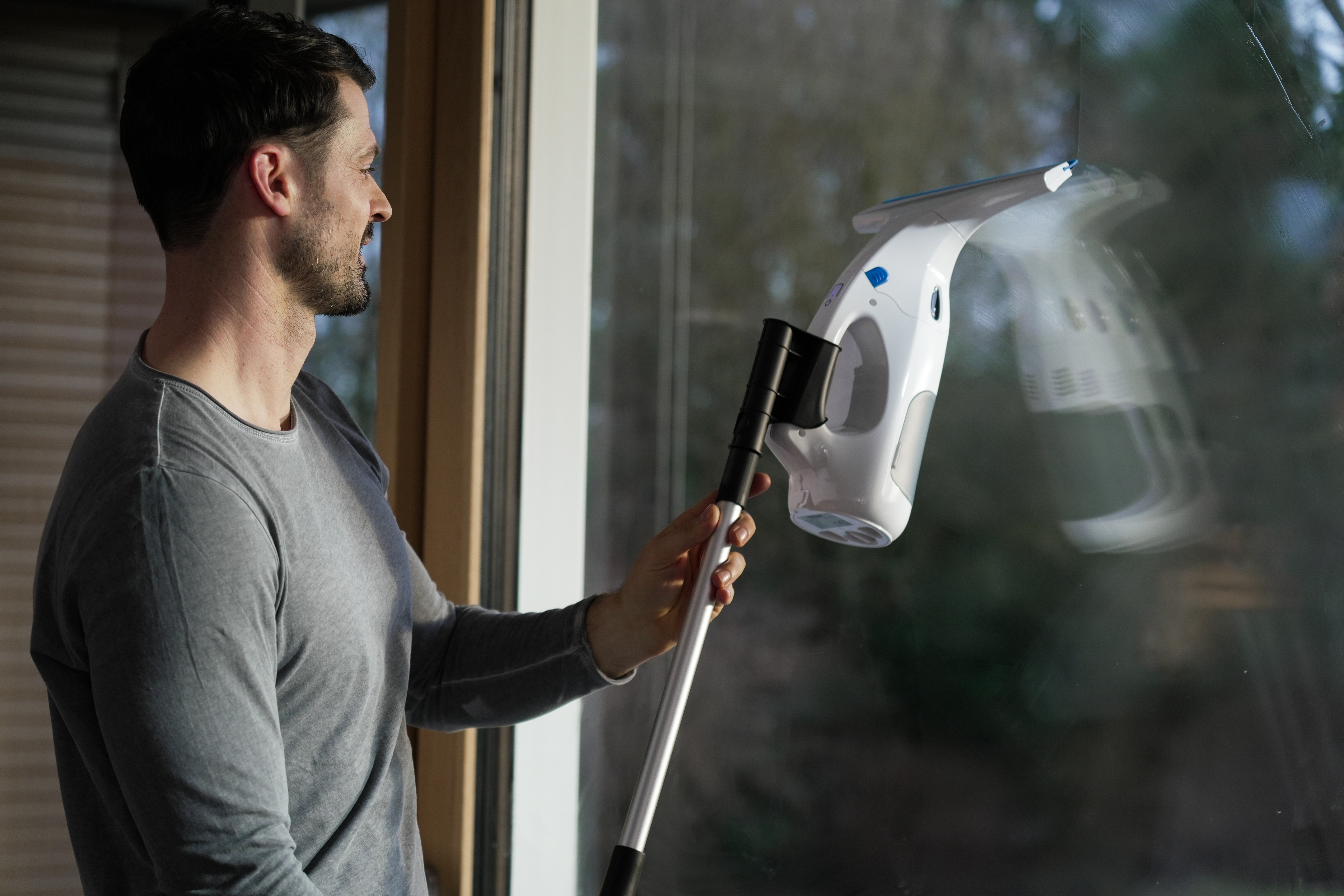 Mann putzt Fenster mit weiß-blauem Reinigungswerkzeug.