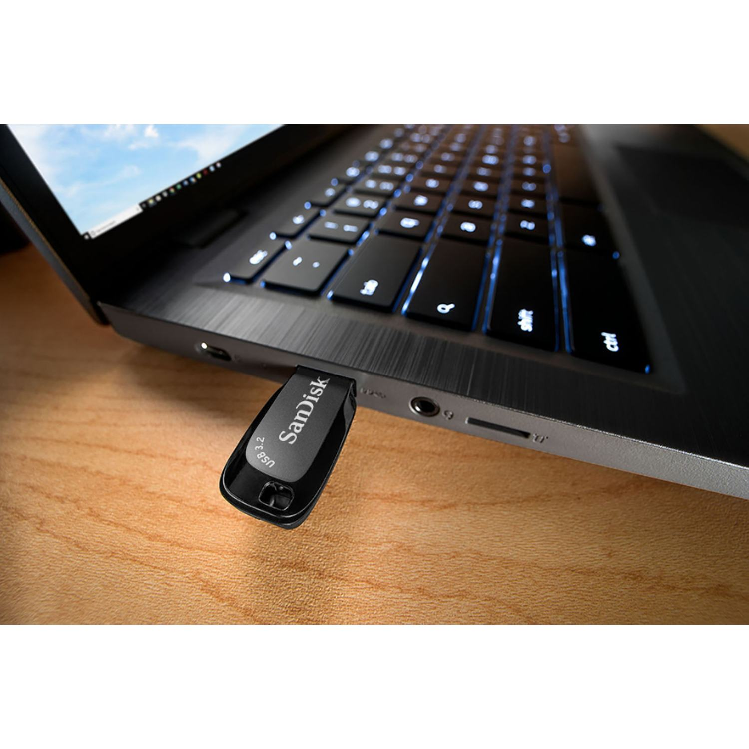 Memoria flash USB negra conectada a una computadora portátil, sobre un escritorio de madera.