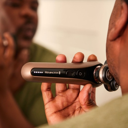 Mężczyzna goli się złotą i czarną golarką elektryczną. Odbicie w lustrze.