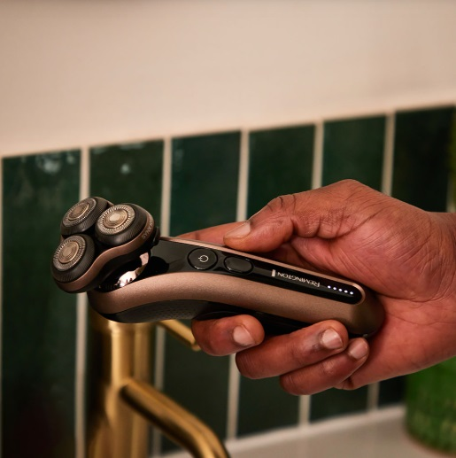 Ręka osoby trzymająca złoto-czarną golarkę elektryczną z trzema obrotowymi głowicami.