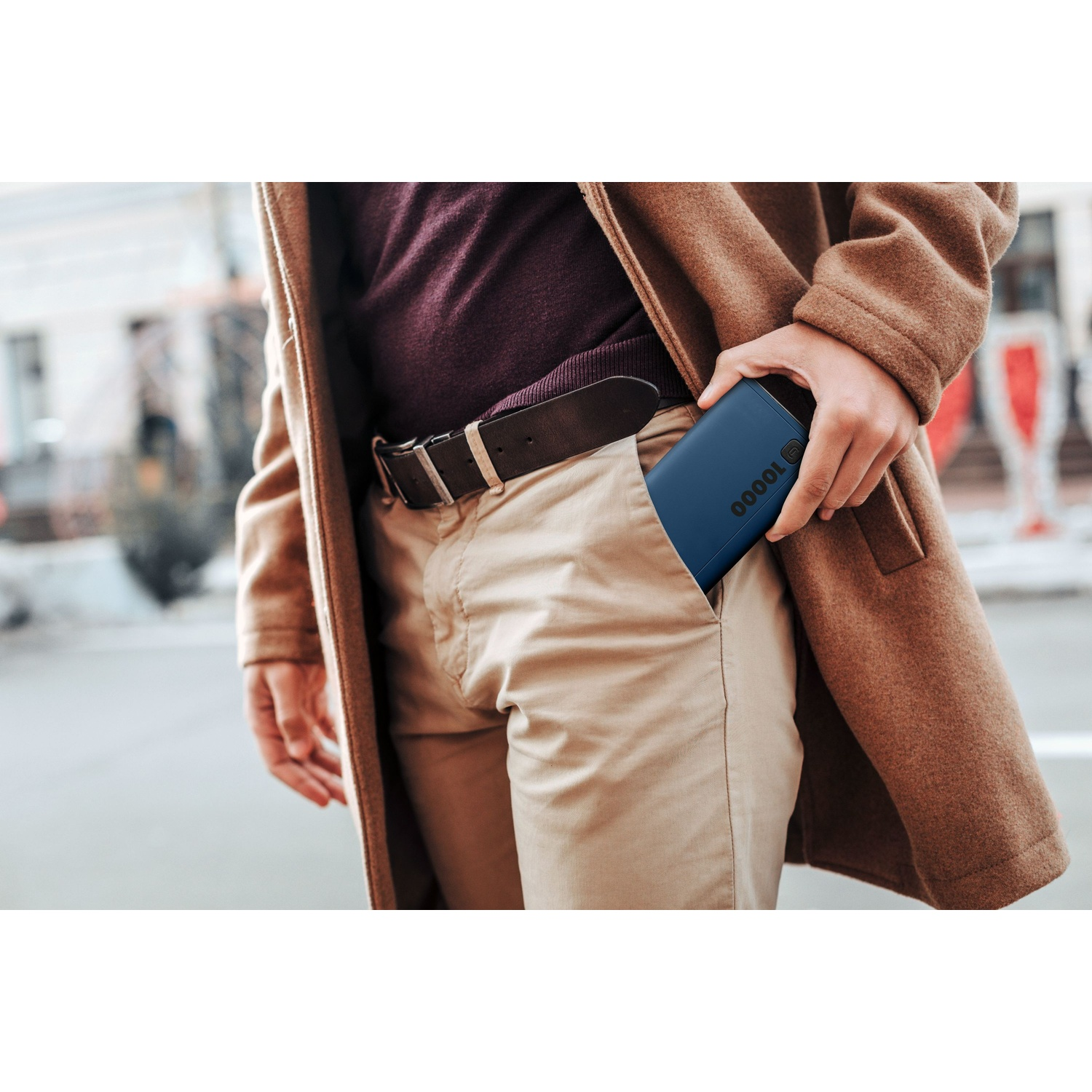Person im braunen Mantel hält eine blaue Powerbank in der Tasche.