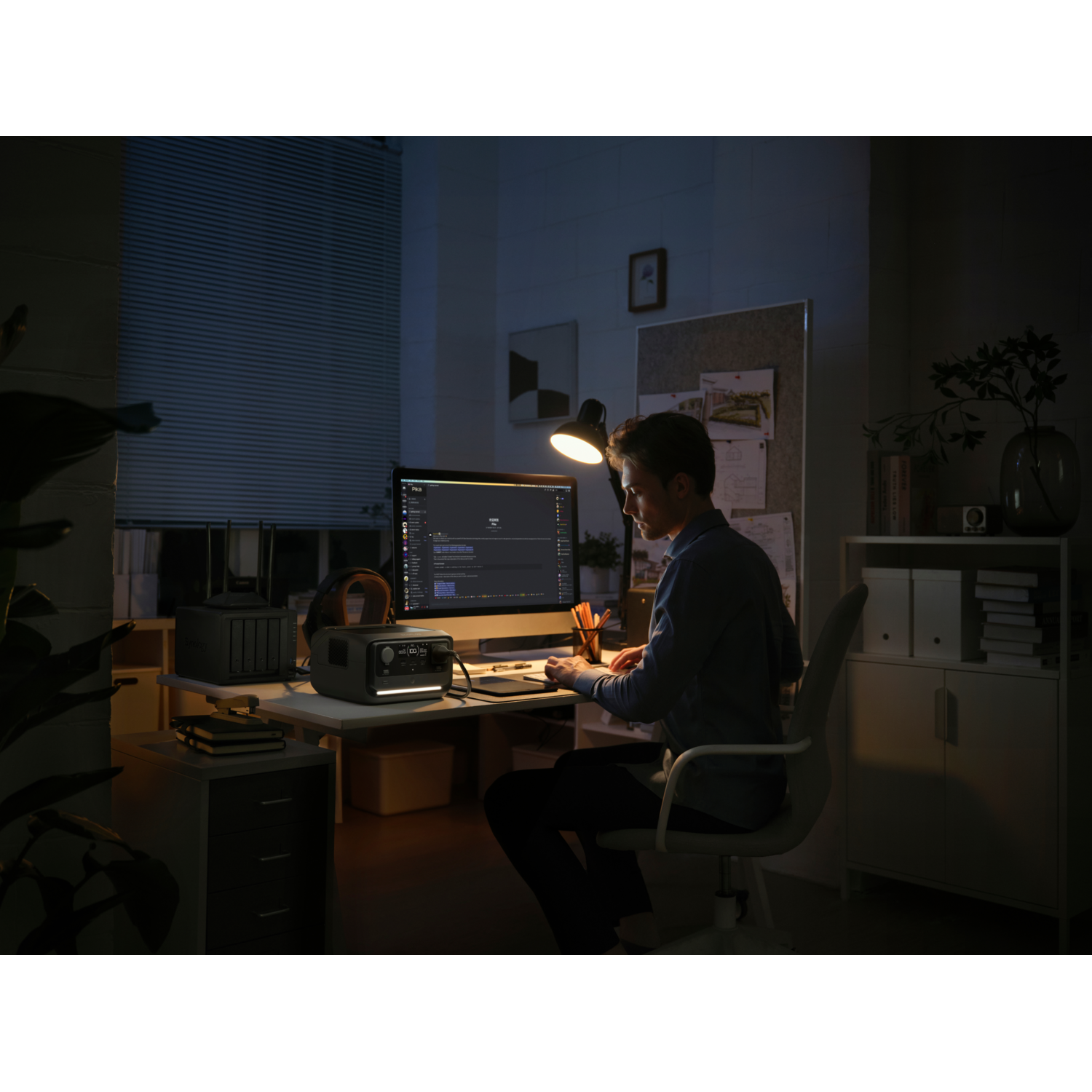 A person at a desk in a dark room, working on a computer.