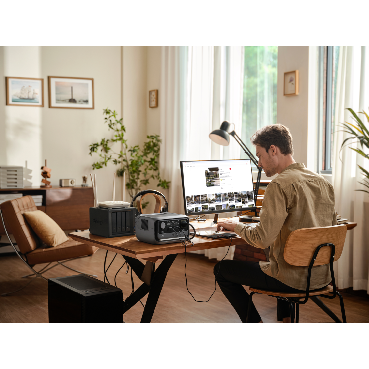 A man is working at a desk with a computer, a router, and a power station.