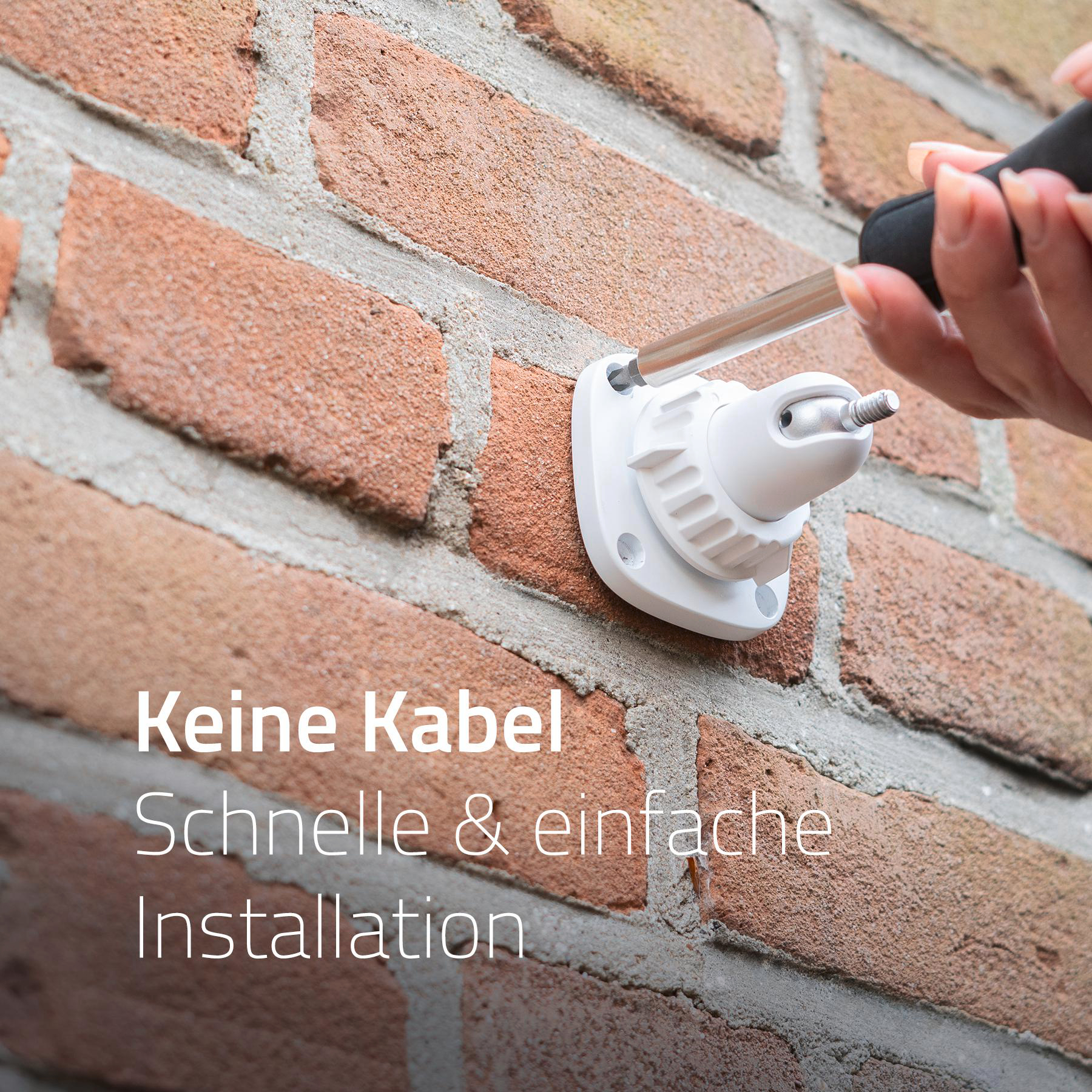 Eine Person, die eine weiße Überwachungskamera an einer Ziegelmauer installiert.