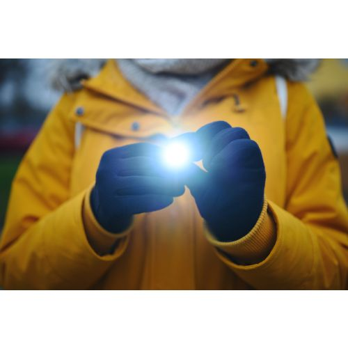 Hände halten eine Taschenlampe, mit hellem Licht, tragen gelbe Jacke.