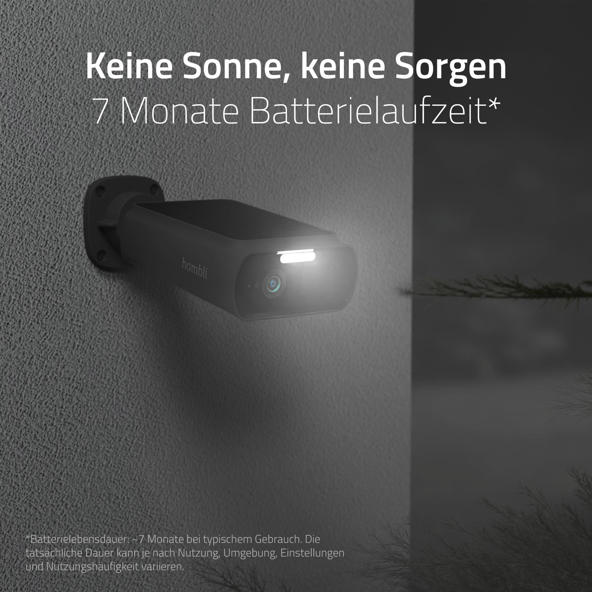 Schwarze Überwachungskamera an einer grauen Wand, mit hellem Licht darauf.