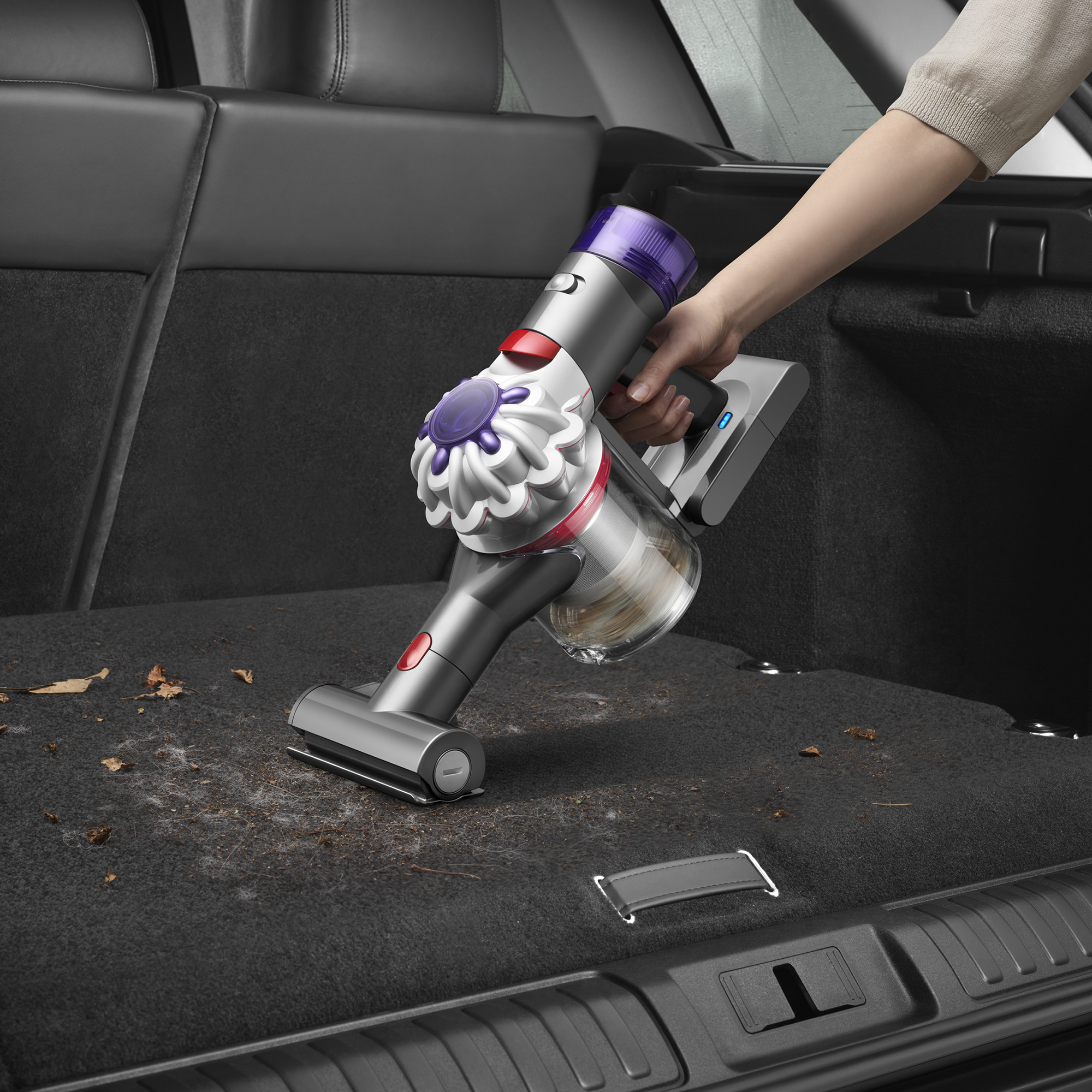 Eine Hand benutzt einen kabellosen Staubsauger im Kofferraum, um Schmutz zu entfernen.