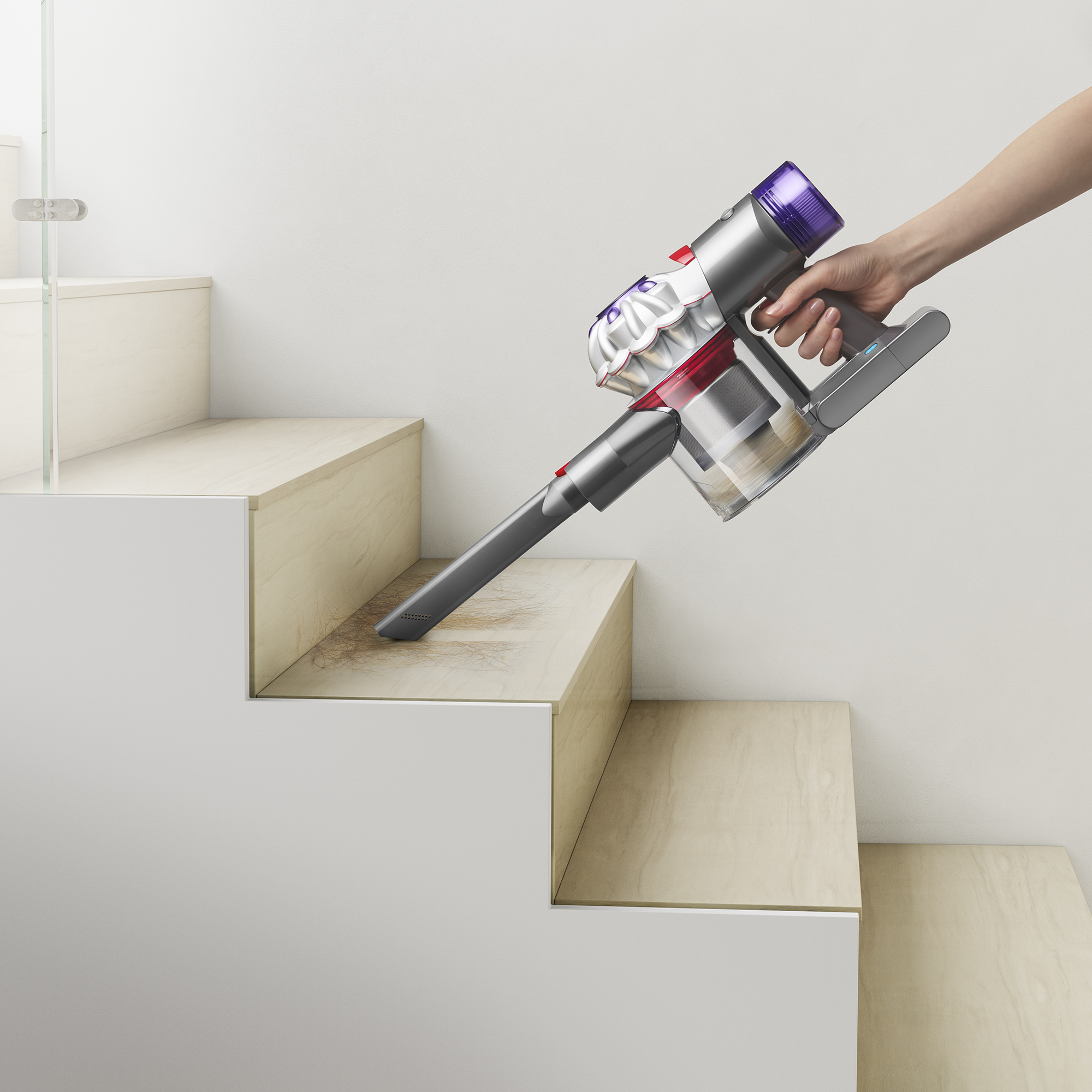 Hand saugt Treppe. Staubsauger rot, weiß, grau. Treppe helles Holz.