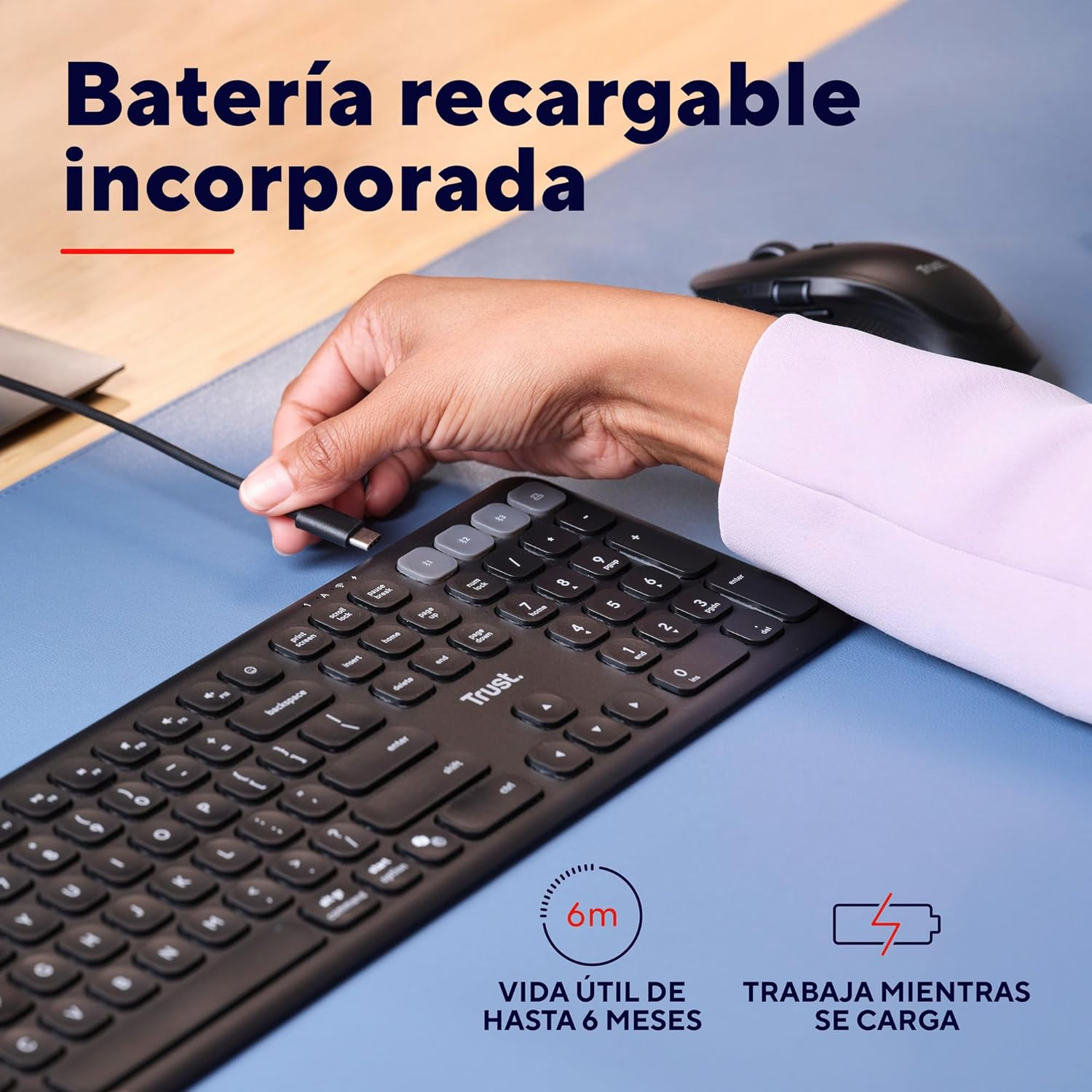 Teclado negro con una mano conectando un cable. Un ratón inalámbrico también en el escritorio.