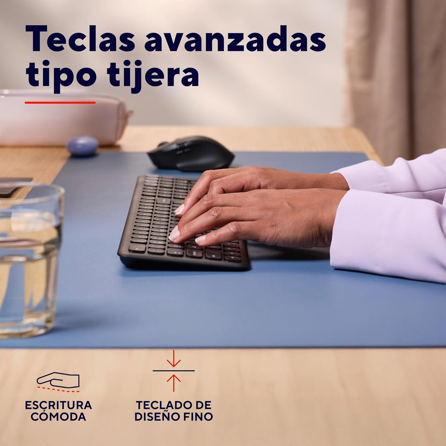 Manos tecleando en un teclado negro sobre una alfombrilla azul, con un vaso de agua y un ratón.