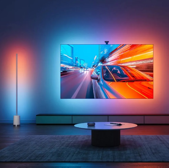 Salon z telewizorem, lampą podłogową i stolikiem. Ściana jest oświetlona.