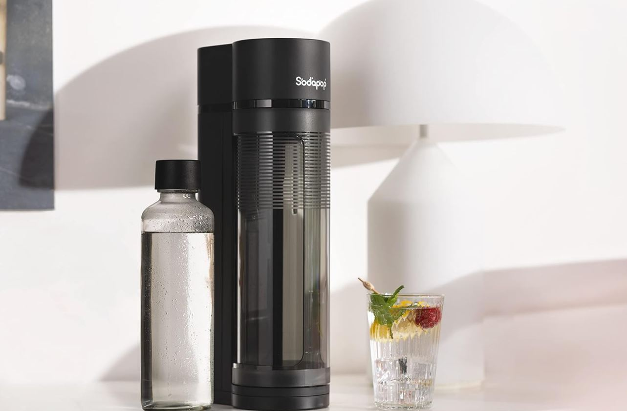 Eine schwarze SodaStream-Maschine mit einer klaren Flasche und einem Glas Soda.