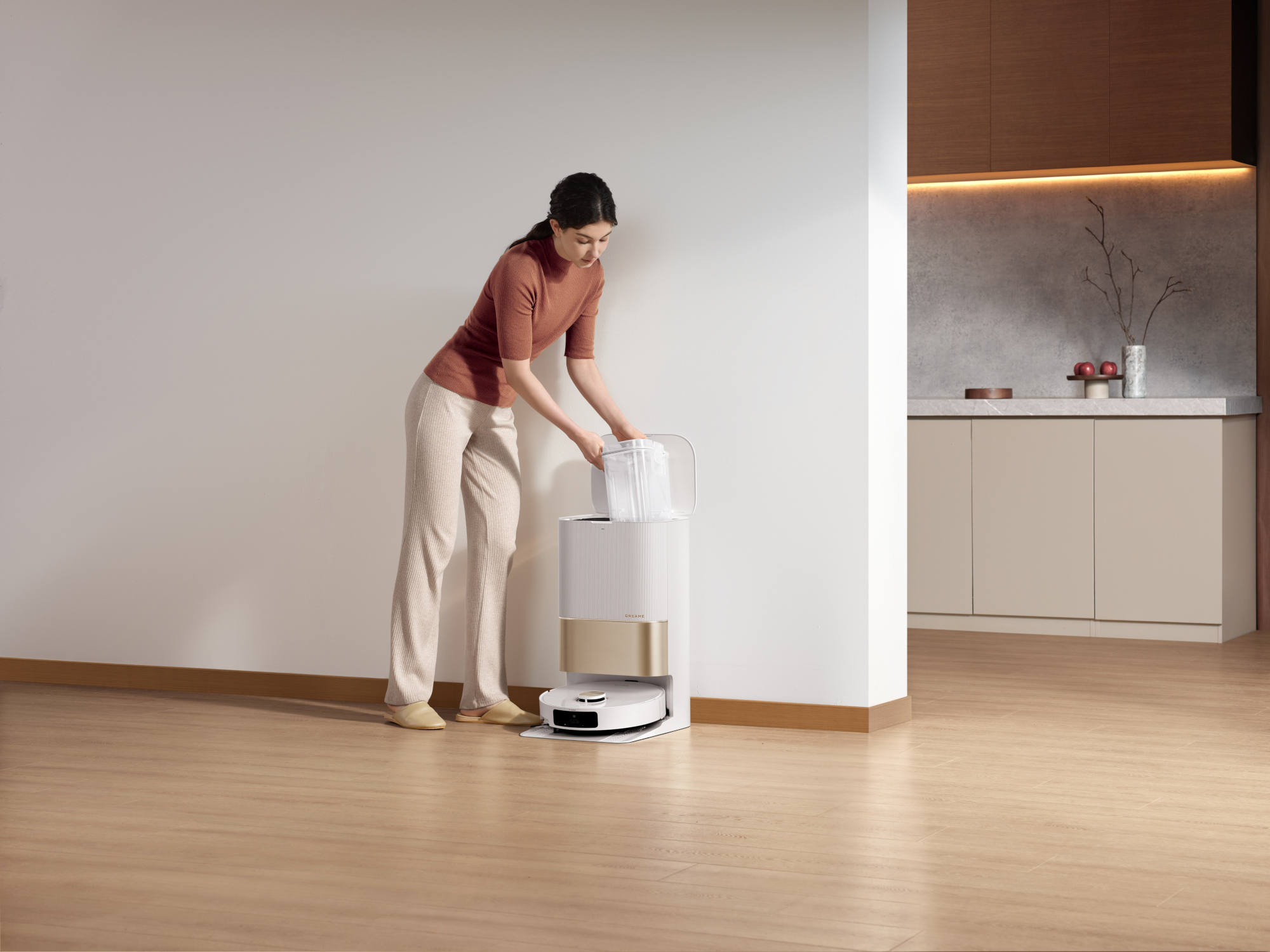 Nő fehér fal közelében, kiüríti a robotporszívó víztartályát.