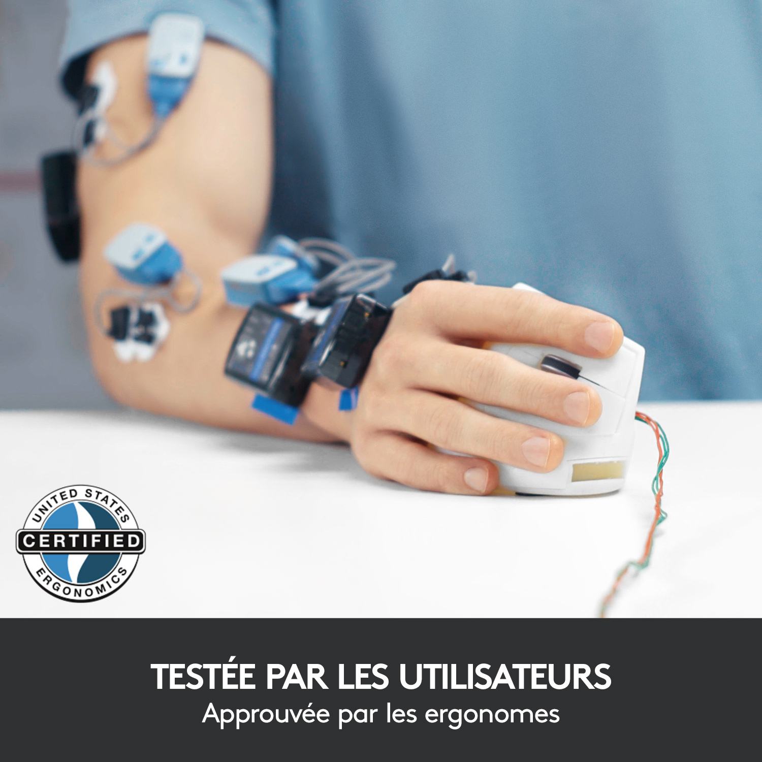 Main avec poignet connecté à des fils, utilisant une souris blanche, sur surface blanche.