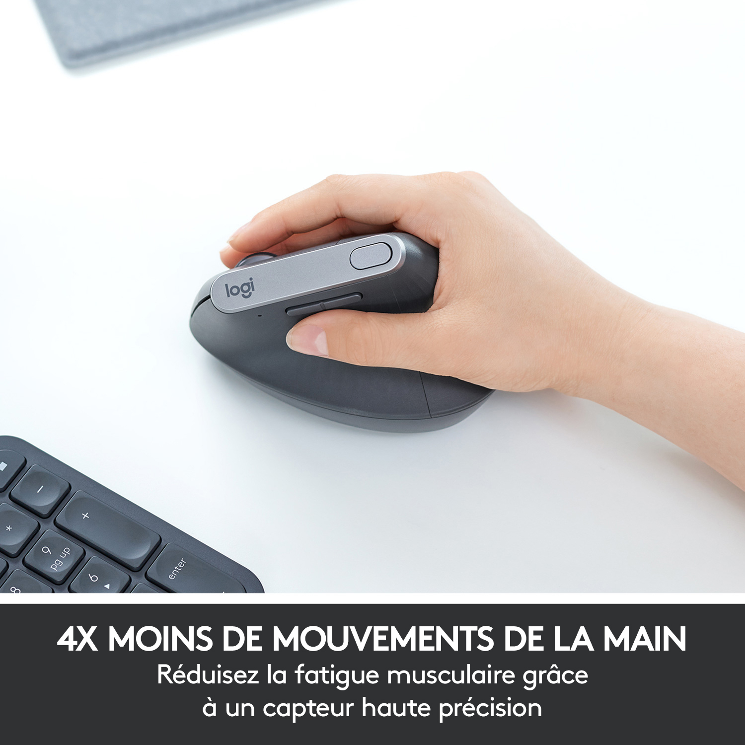Main utilisant une souris grise, sur une surface blanche, avec un clavier en arrière-plan.