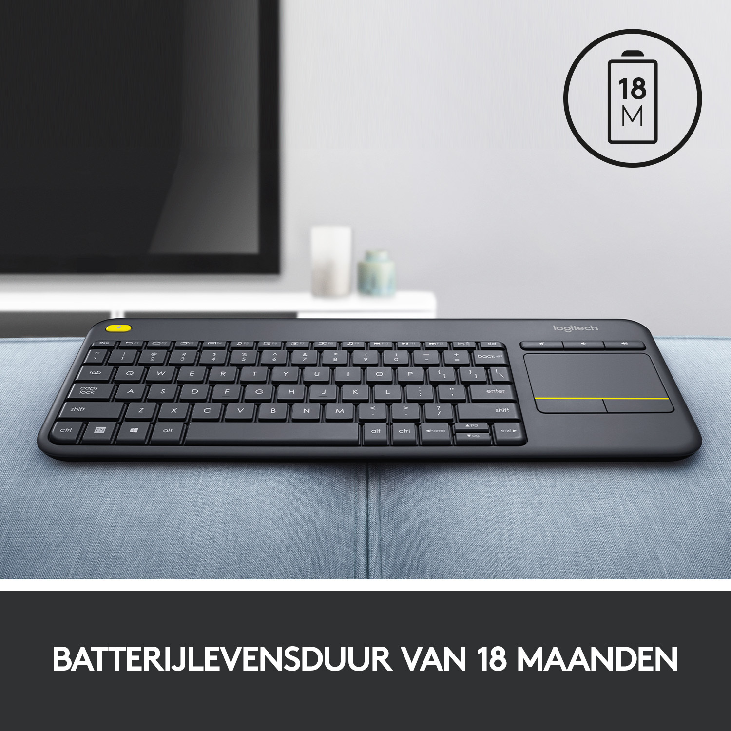 Black keyboard with a touchpad, next to a TV on a blue couch.