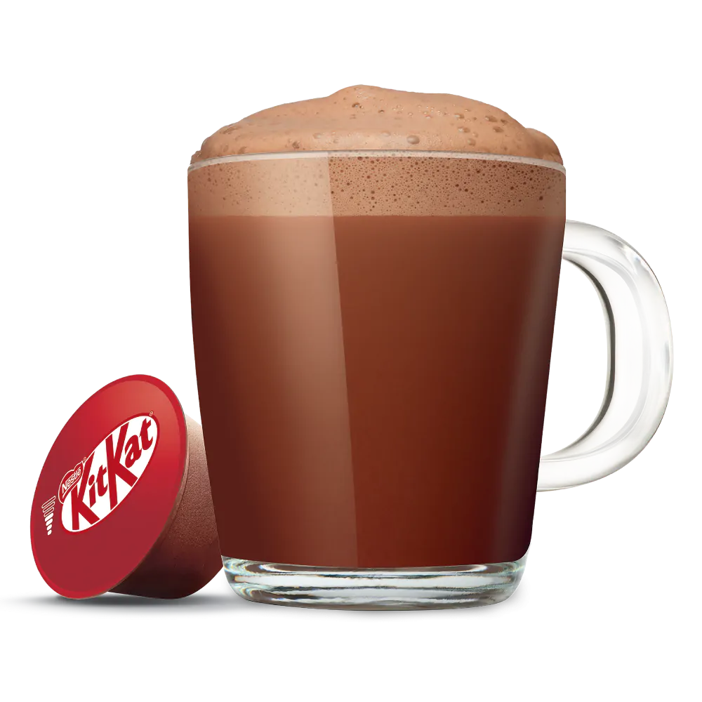 Una taza de vidrio de chocolate caliente con espuma y un envoltorio de caramelo KitKat rojo.