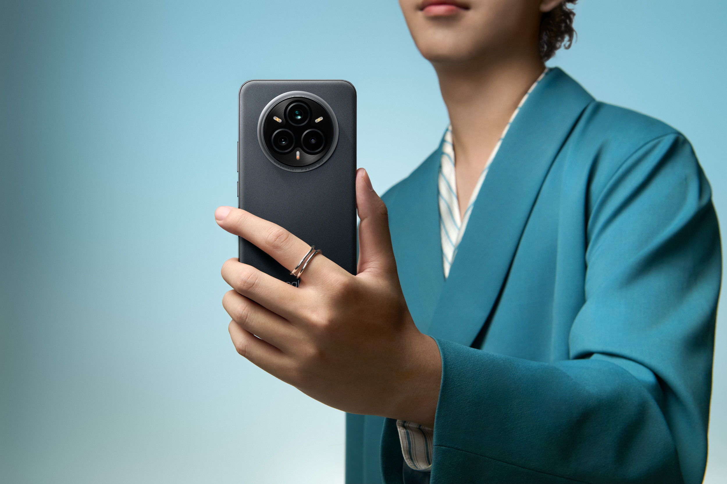 Mężczyzna trzyma ciemny telefon, pokazując jego aparat, na niebieskim tle.