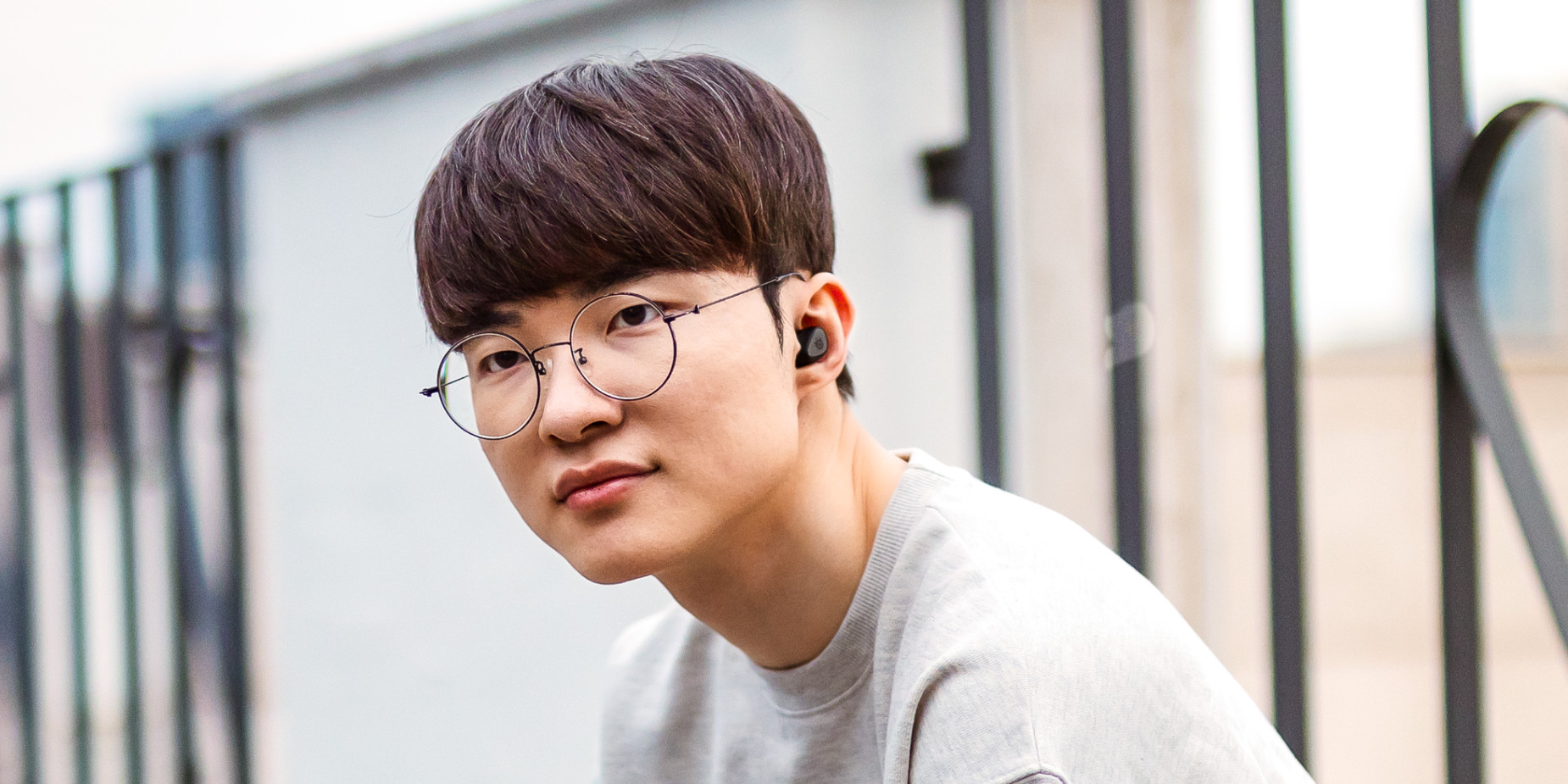 Młody mężczyzna w okularach i słuchawkach. Patrzy w kamerę i uśmiecha się, w jasnoszarej koszuli.